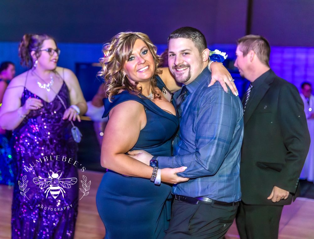 Couples dancing at formal event with blue ambient lighting and wooden floor.