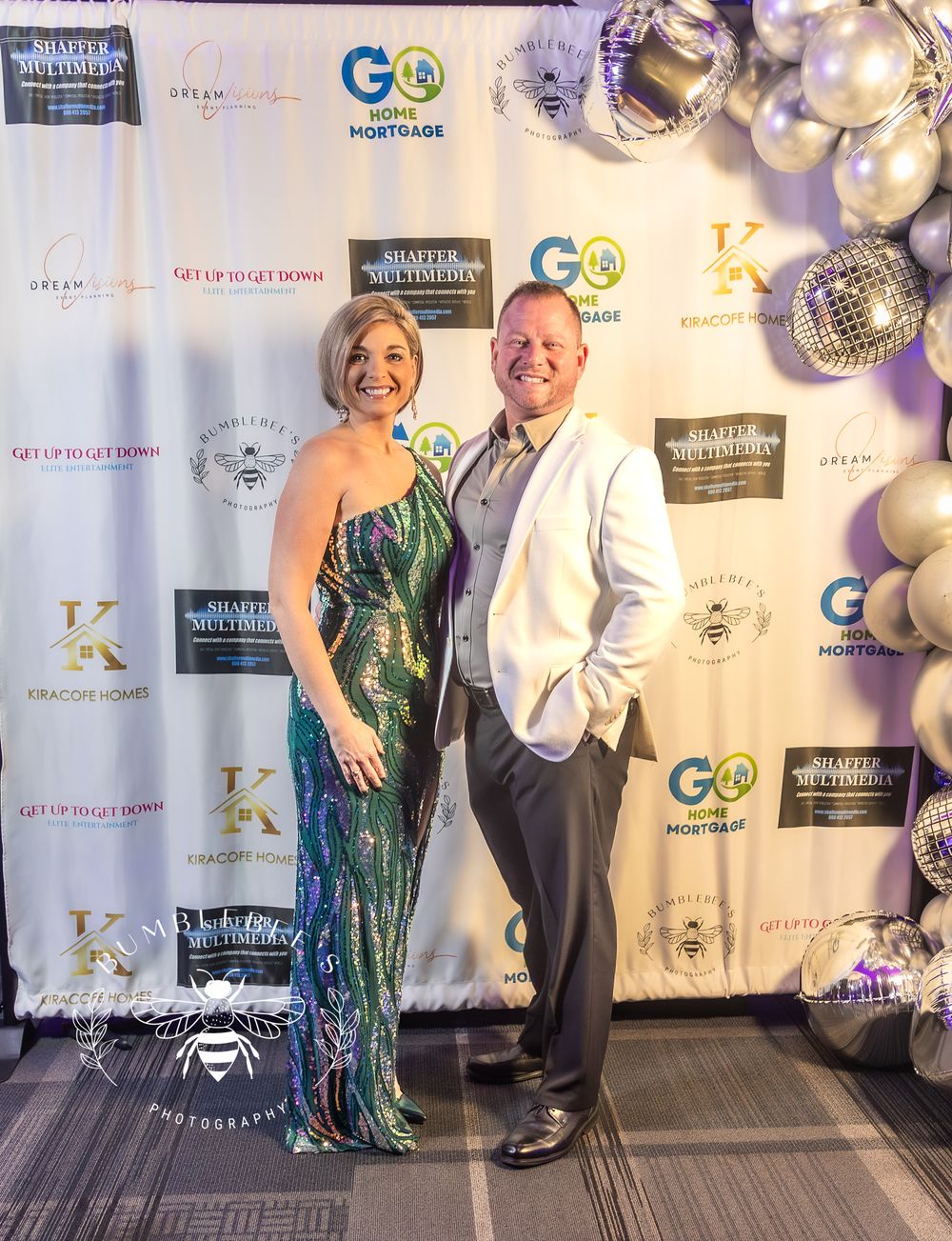 Elegant couple poses at formal gala event with sparkly decorative balloon display.