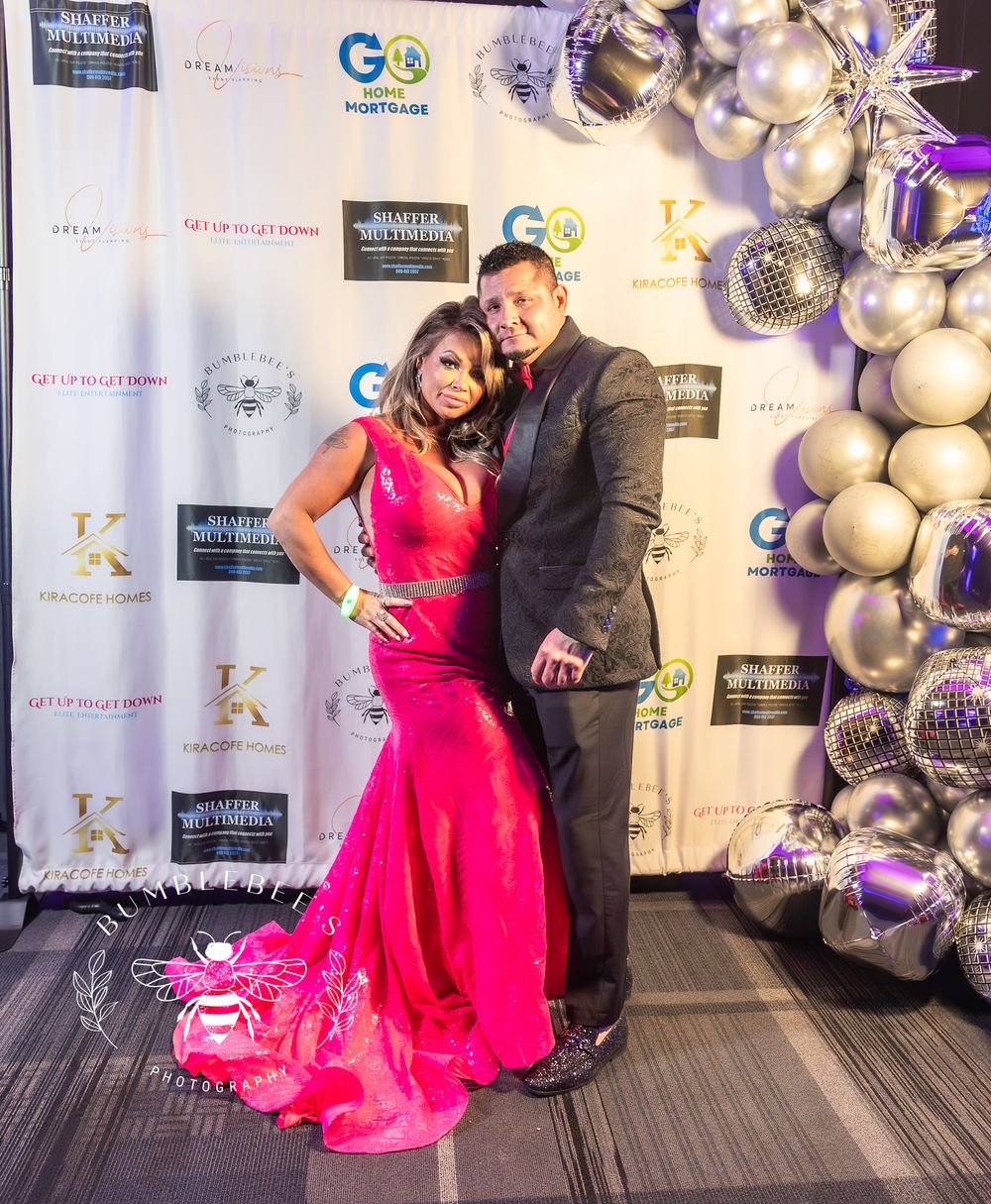 Formal event photograph with couple posing against branded backdrop with silver balloon decor.