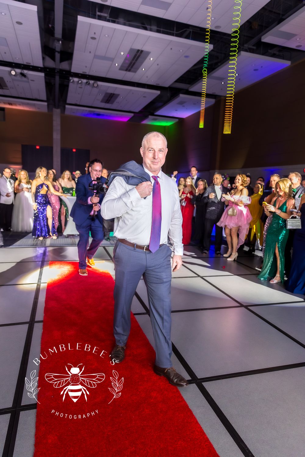 A person in a suit and pink tie strikes a pose on a red carpet at a party.