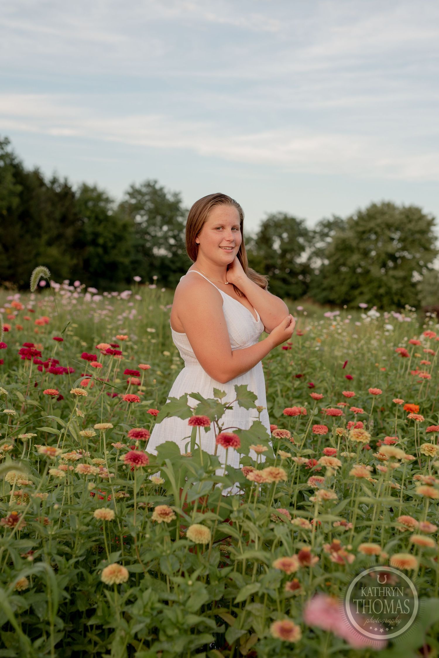 Person in white sundress poses among colorful summer wildflowers in a garden.