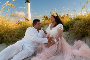 Couple sharing tender moment in beach dunes during golden hour maternity photo session.