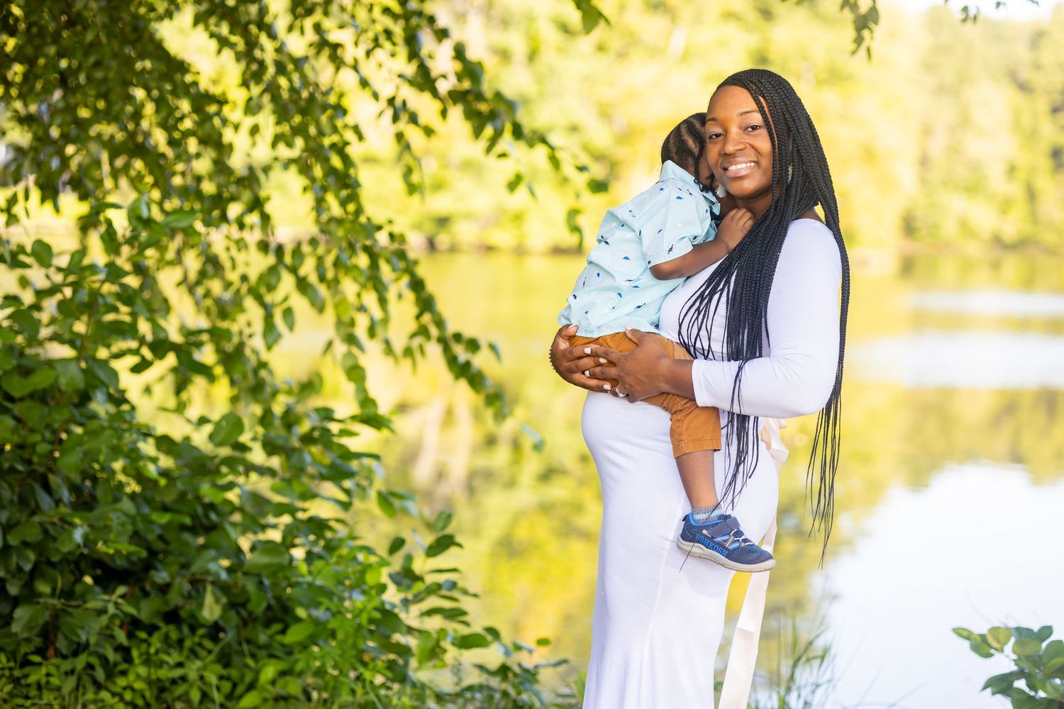 Outdoor portrait of mother and baby in white dress against natural lake background.