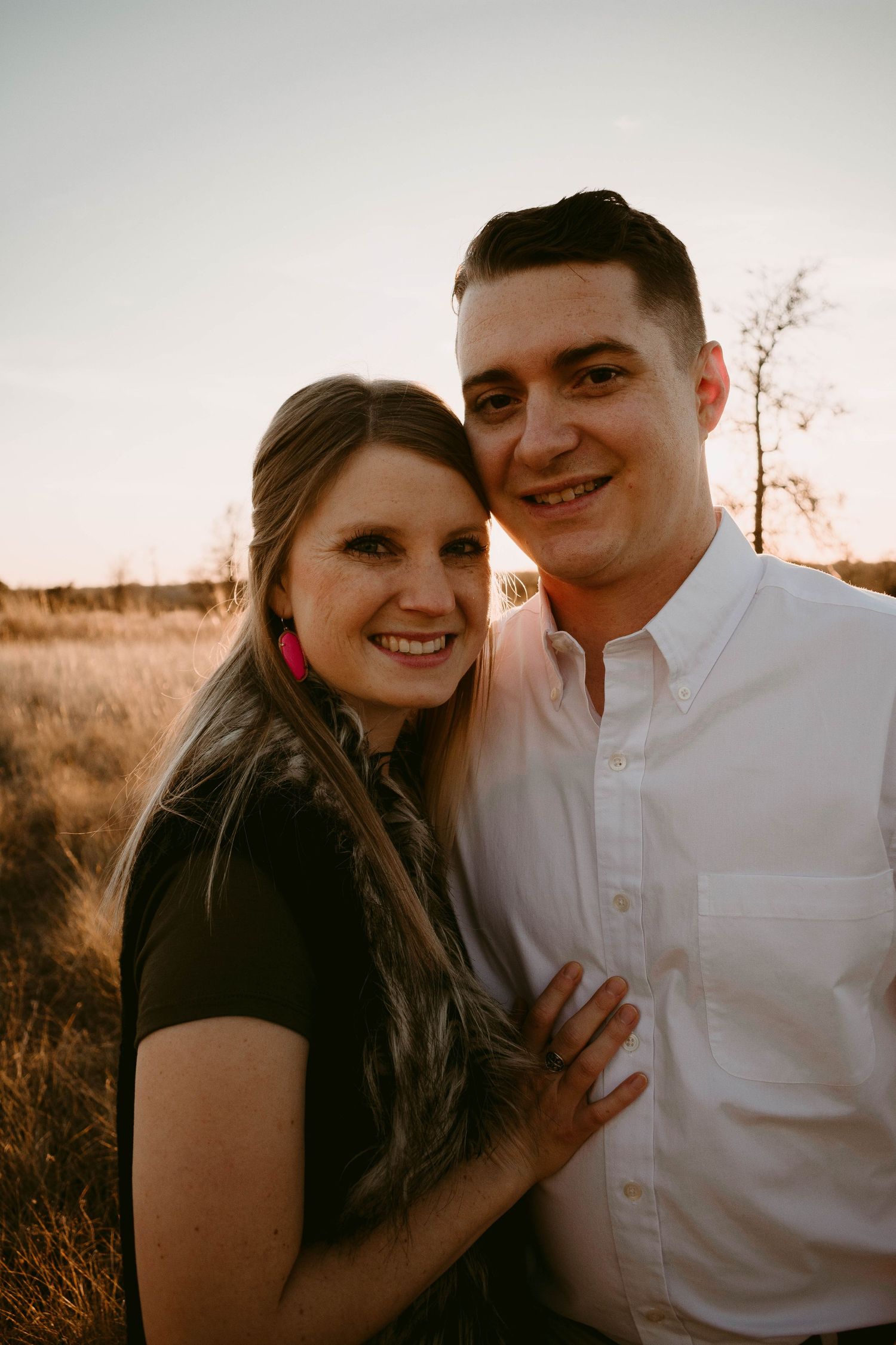 Close-up portrait of a couple in coordinated black and white outfits against a sunset landscape.