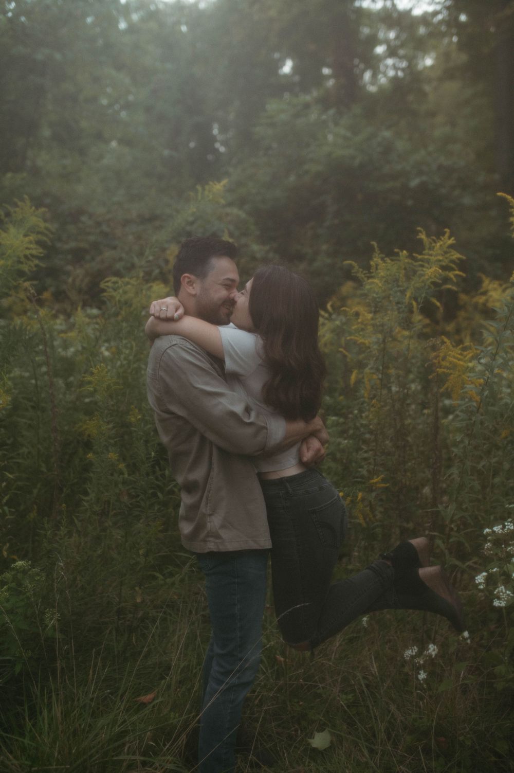 A playful romantic moment between a couple in a natural outdoor setting with golden flowers.