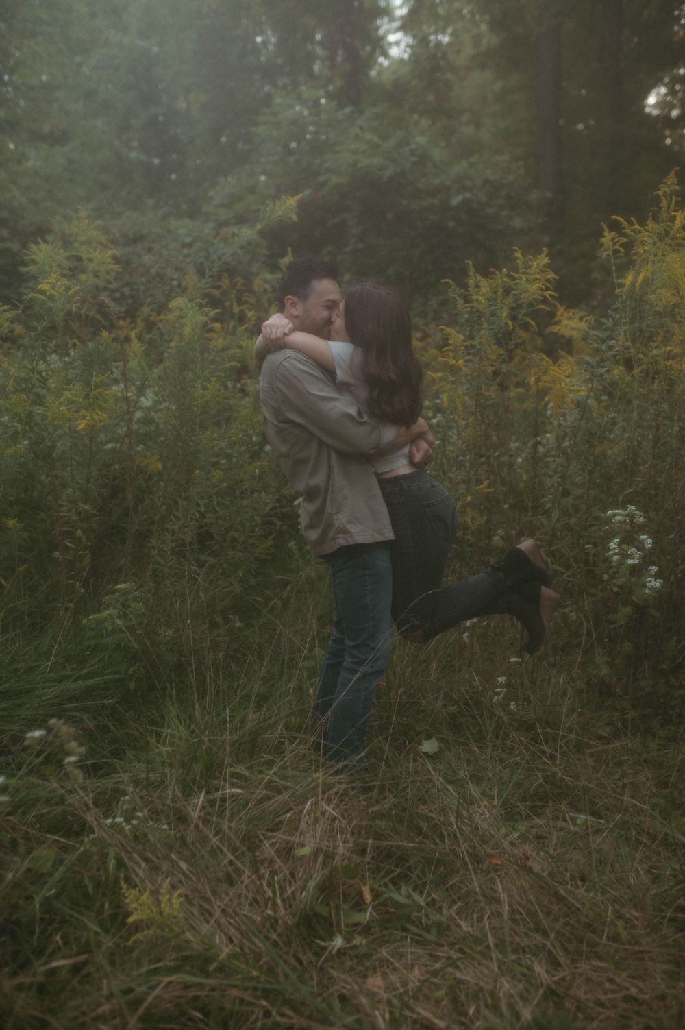 A joyful couple embracing in a meadow with yellow wildflowers and forest backdrop.