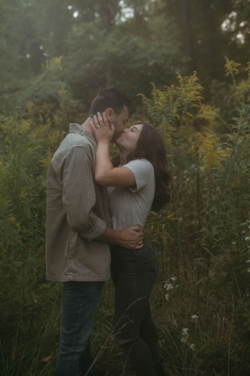 An intimate outdoor portrait of a couple kissing among tall wild grasses and yellow flowers.