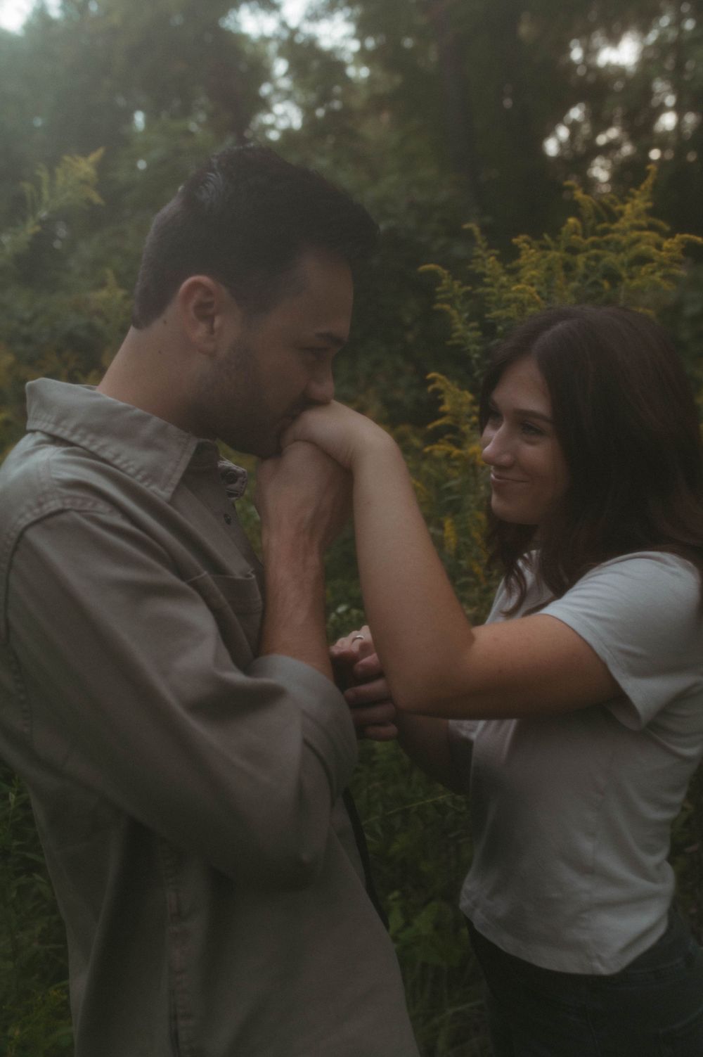 Romantic outdoor engagement photo with couple in casual wear among wildflowers.