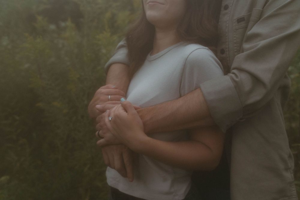 Intimate embrace captured in moody lighting with couple's hands intertwined.