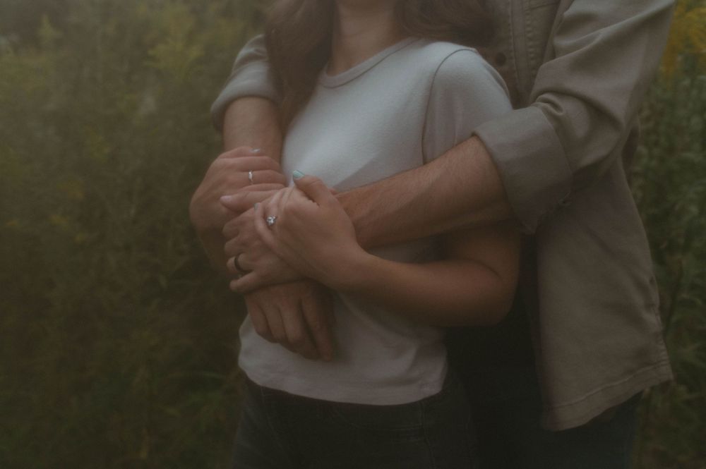 Close-up shot of couple embracing in casual attire against natural background.