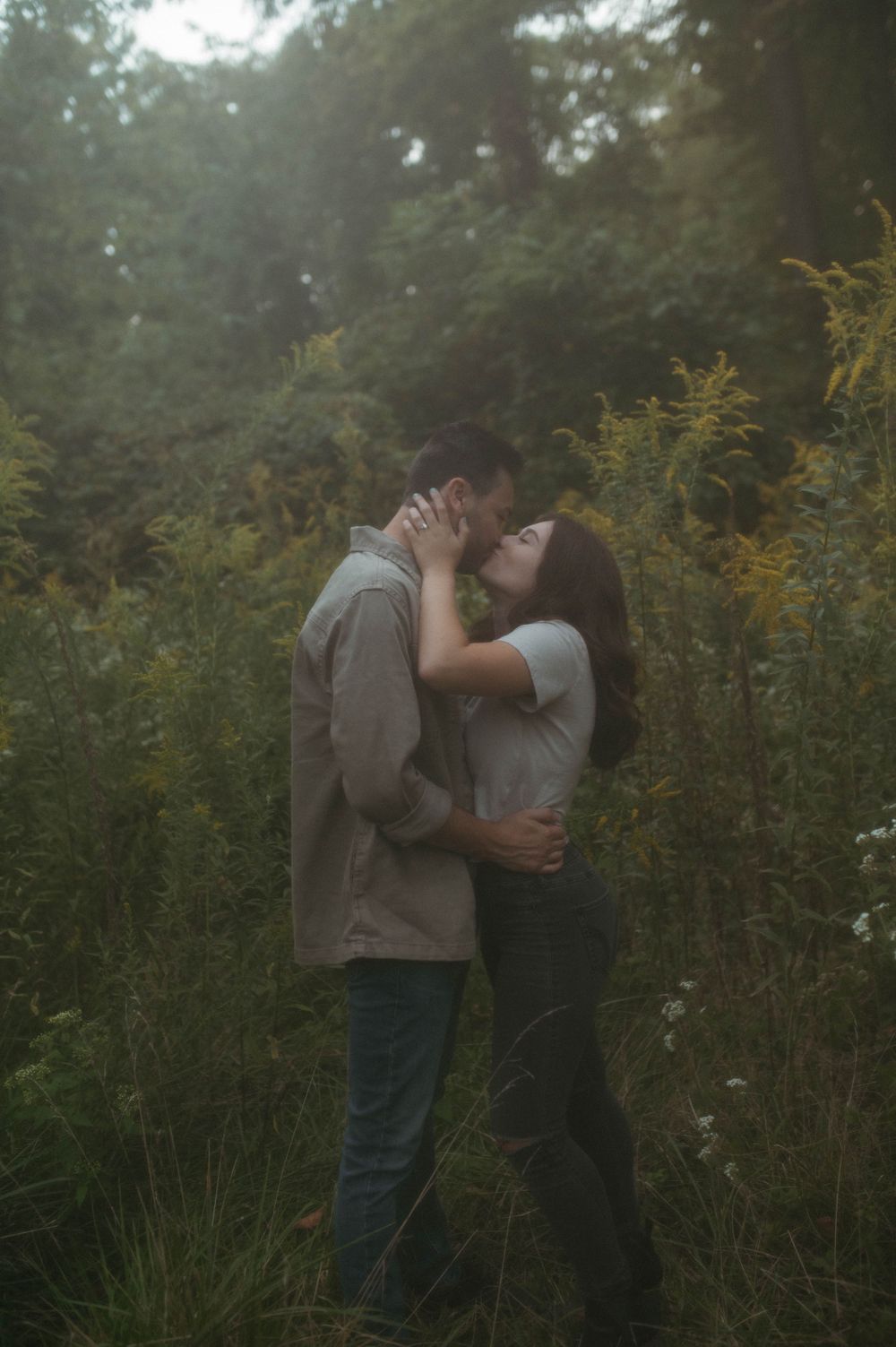 A loving embrace captured in a misty outdoor setting with yellow flowers in the background.