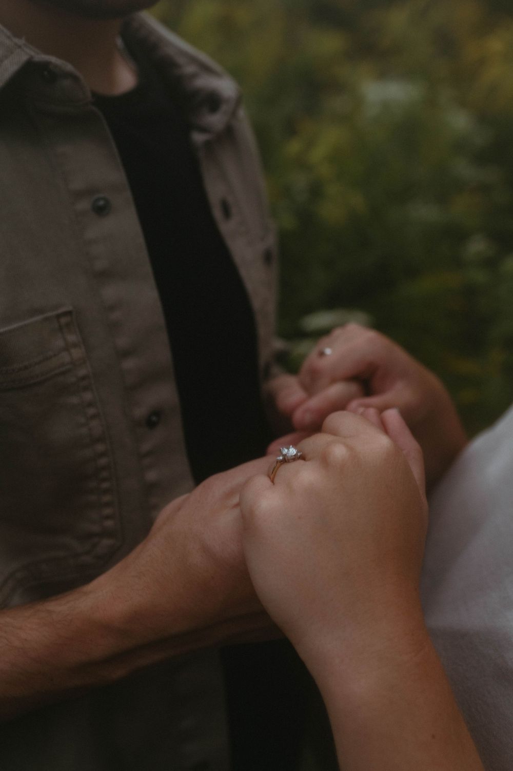 Close-up of hands displaying engagement ring in romantic outdoor setting.