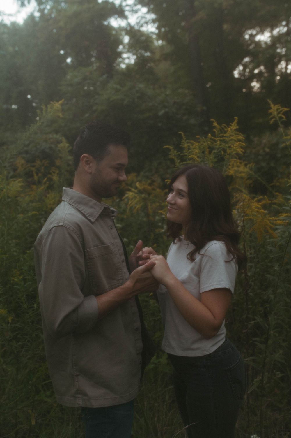 Couple shares tender moment while holding hands in field of golden wildflowers at dusk.