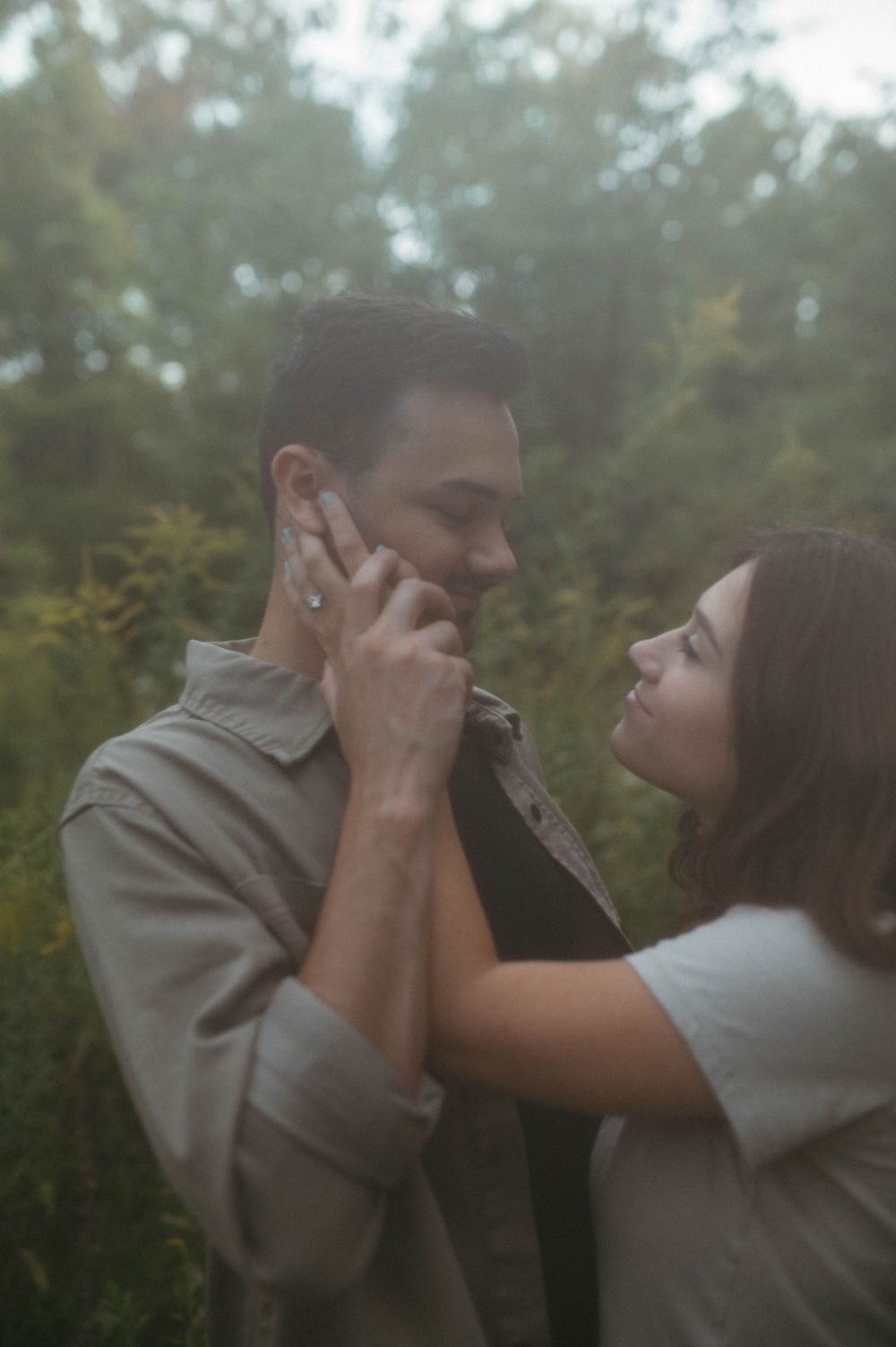 A tender moment between a couple in casual attire surrounded by autumn foliage.