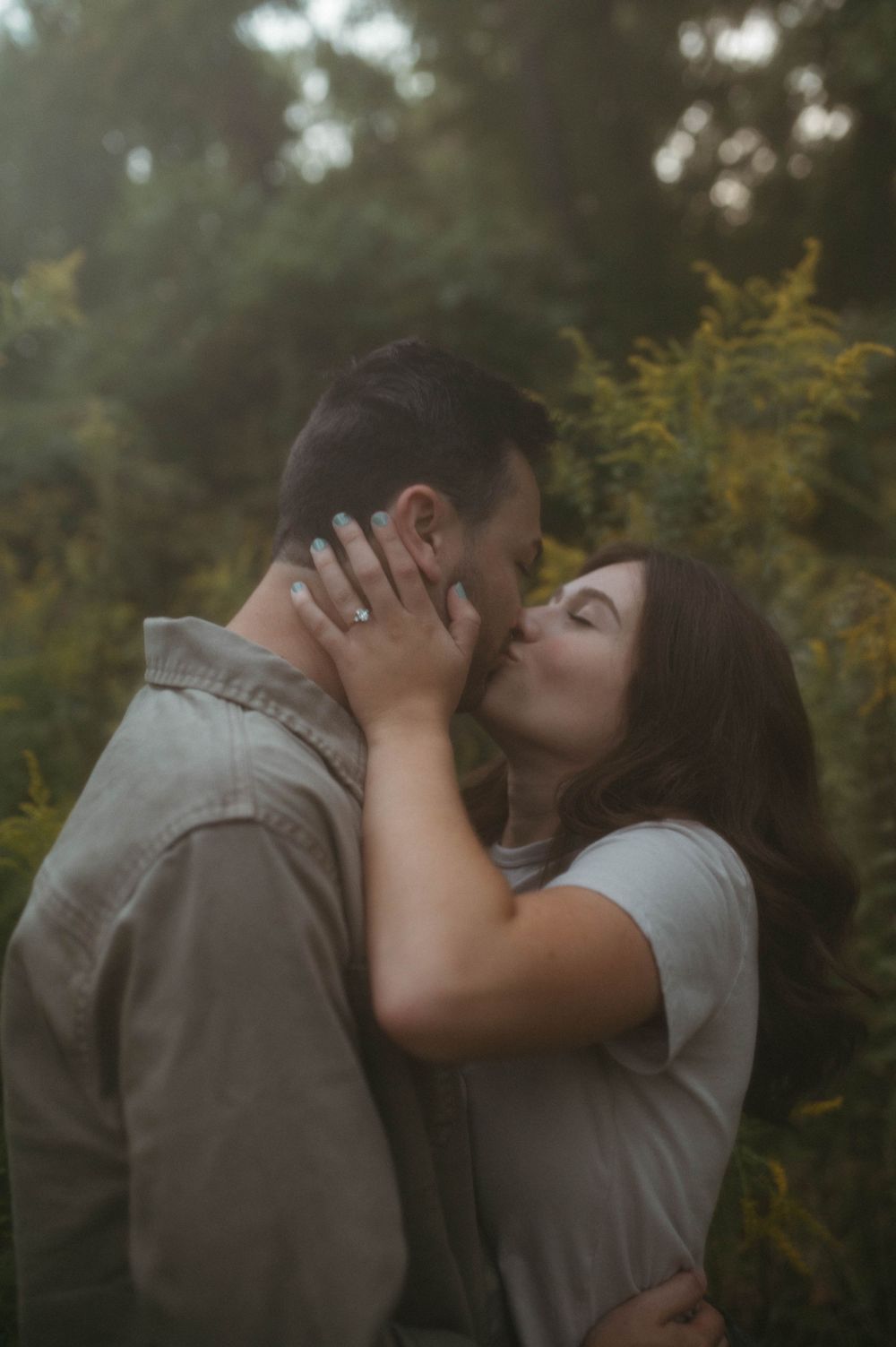 A romantic couple sharing an intimate moment amidst golden wildflowers in a dreamy outdoor setting.