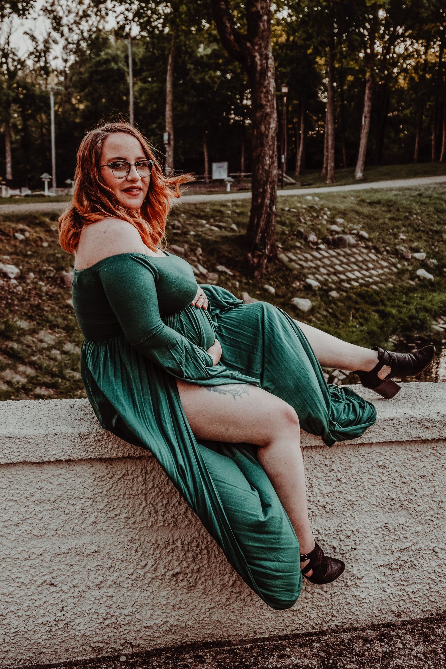 Graceful maternity portrait in an emerald dress against a natural outdoor setting.