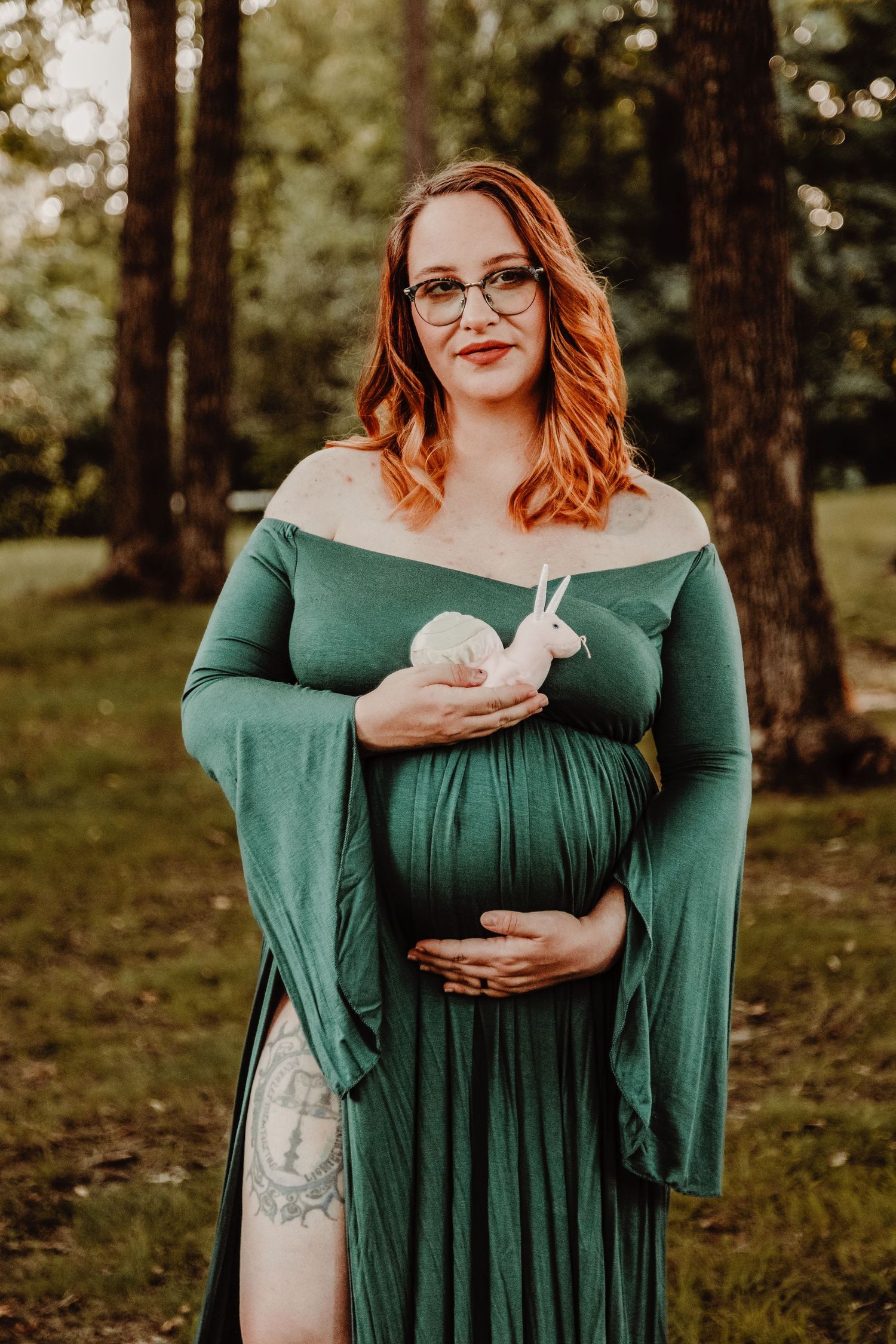 Maternity portrait in a forest setting featuring an elegant green off-shoulder dress.