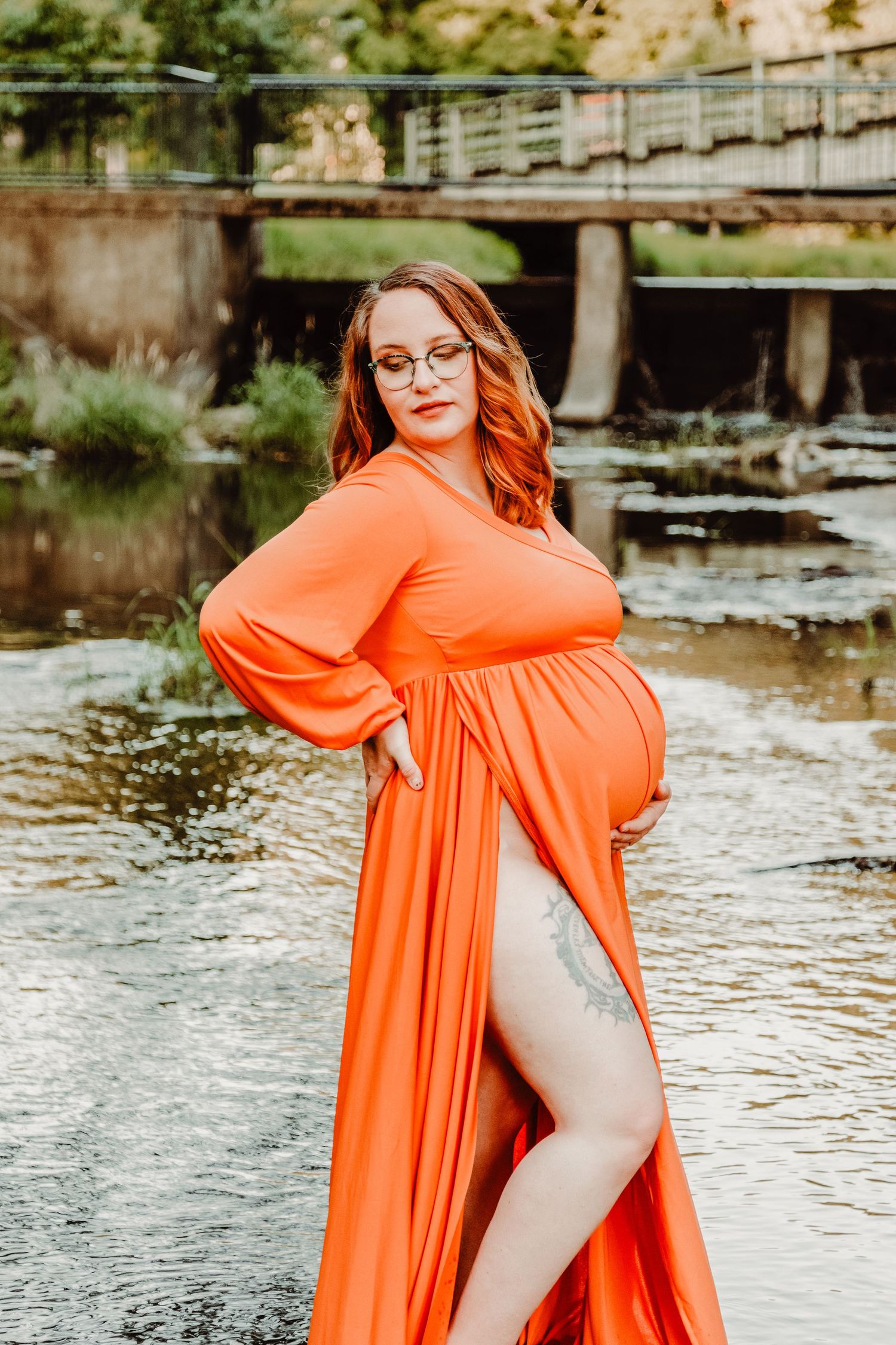 Vibrant orange maternity dress creates striking contrast against a peaceful waterfront backdrop.