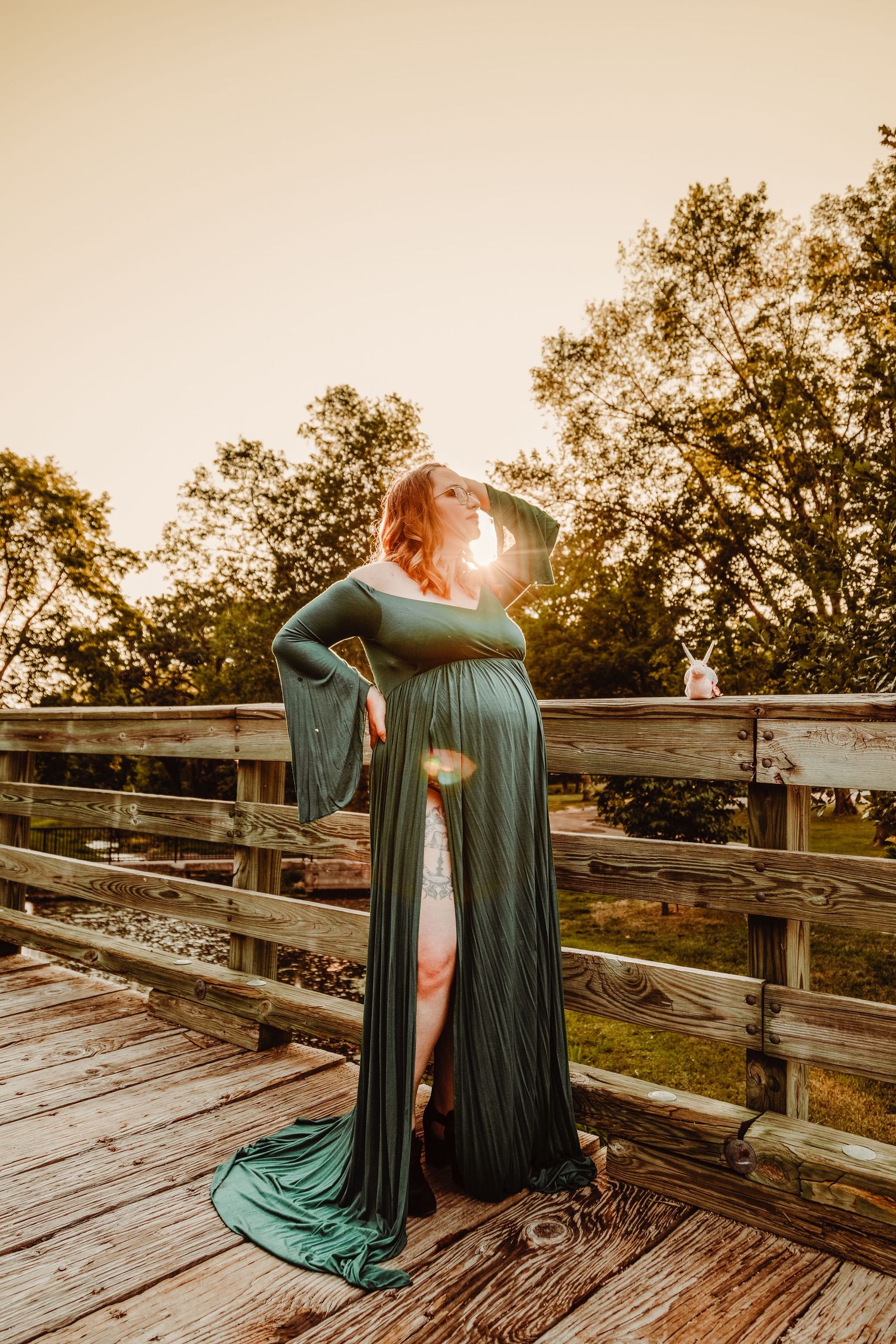 Elegant maternity photo of a teal dress flowing in golden sunset light on a wooden deck.