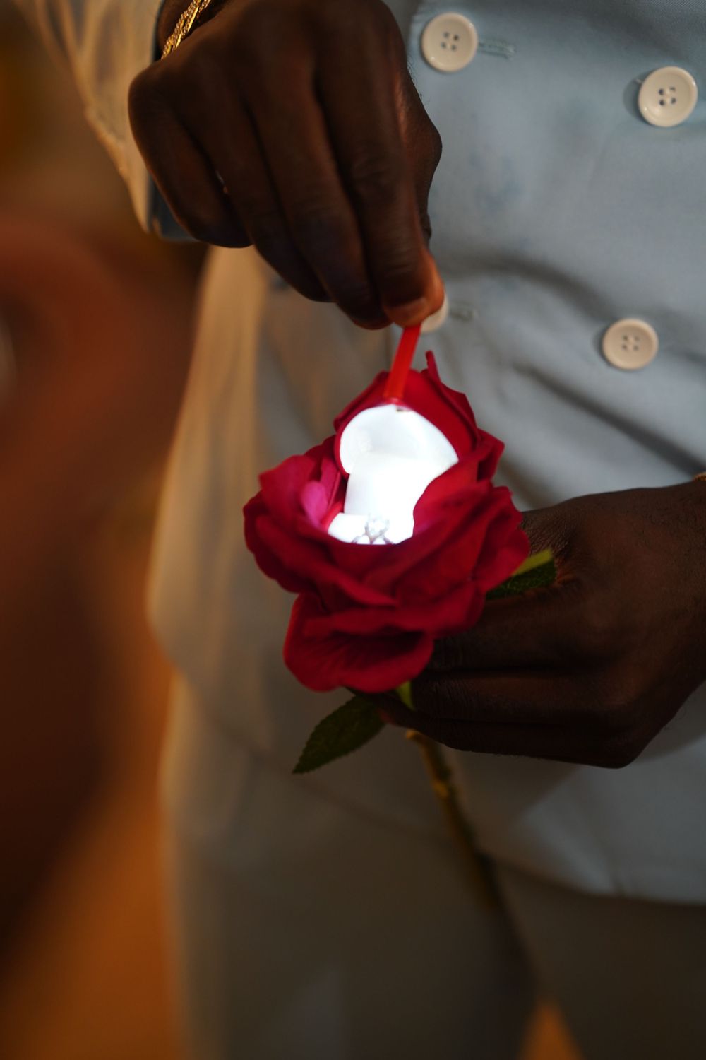 Close-up of hands holding a red rose with an illuminated light inside the petals.
