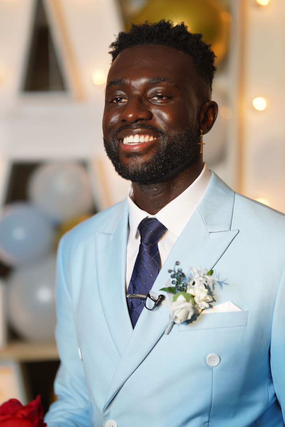 A formal portrait showing elegant light blue suit with boutonniere against illuminated background.