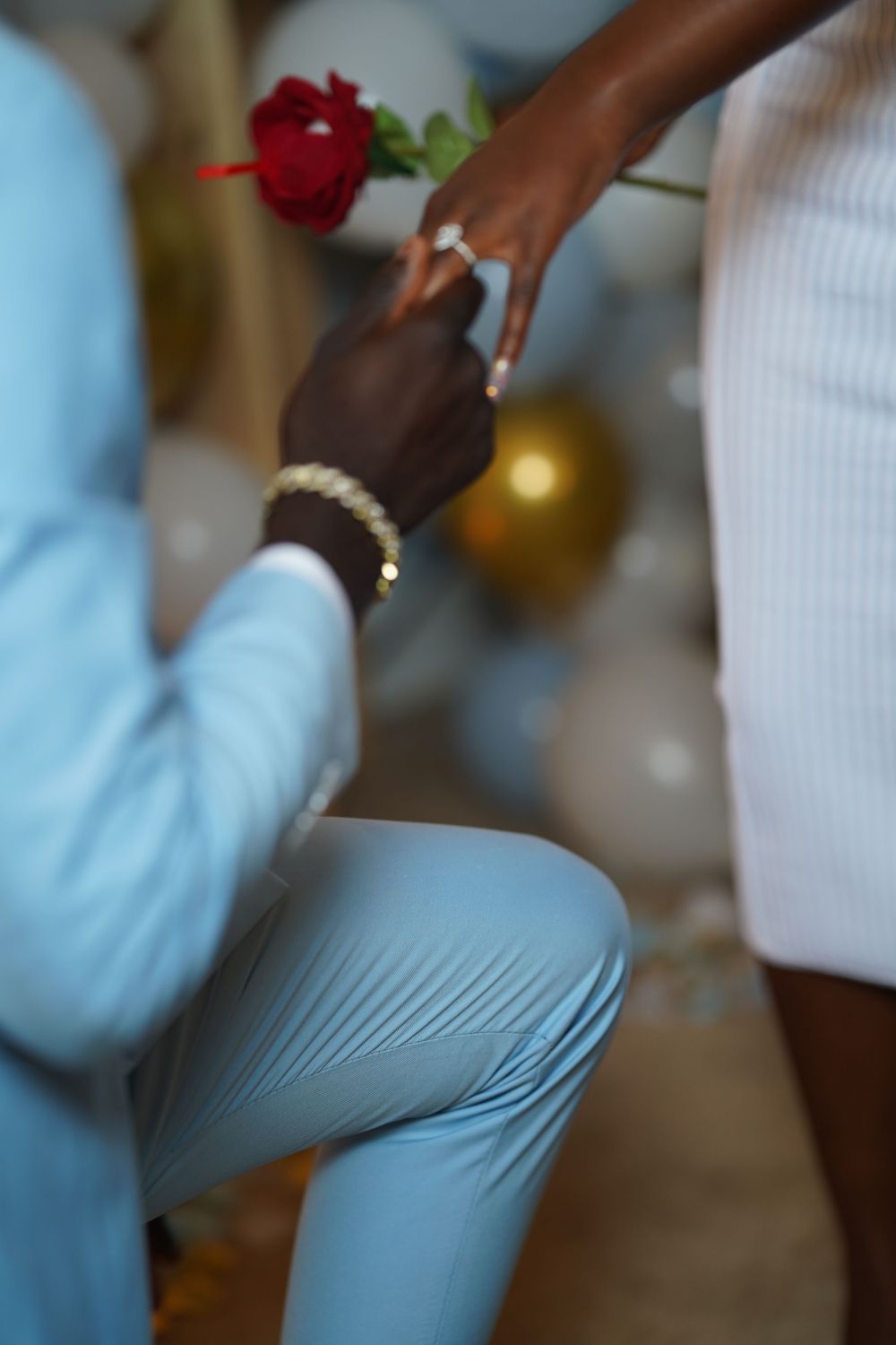 Close-up of hands during proposal with a single red rose and light blue suit sleeve.