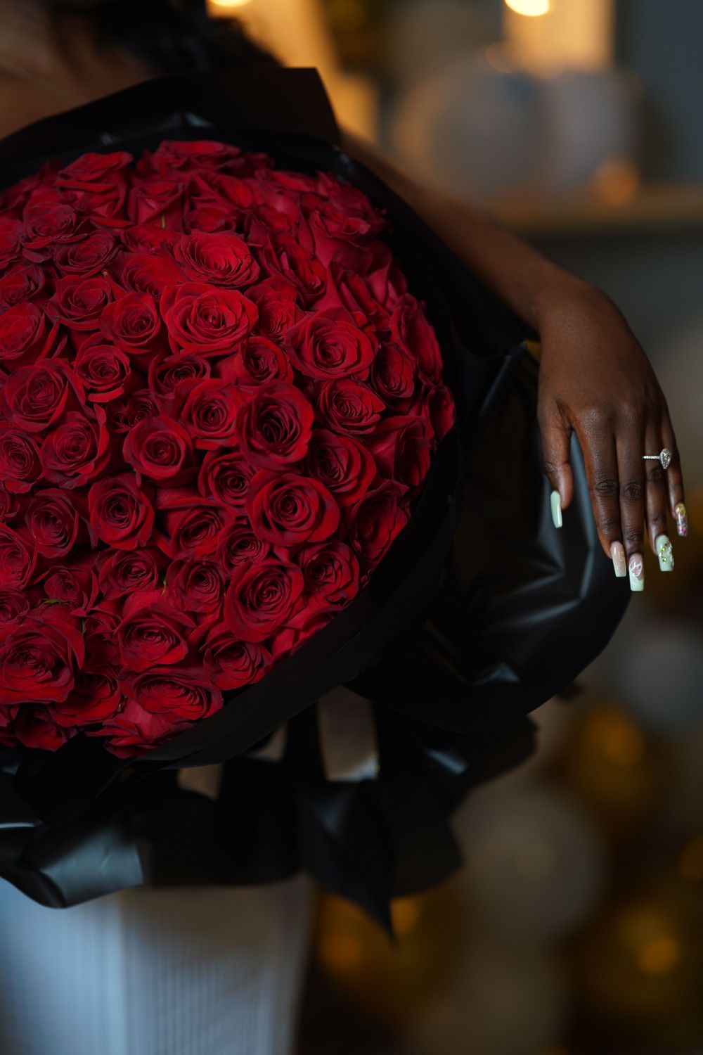 A large bouquet of vibrant red roses wrapped in black paper with a manicured hand visible.