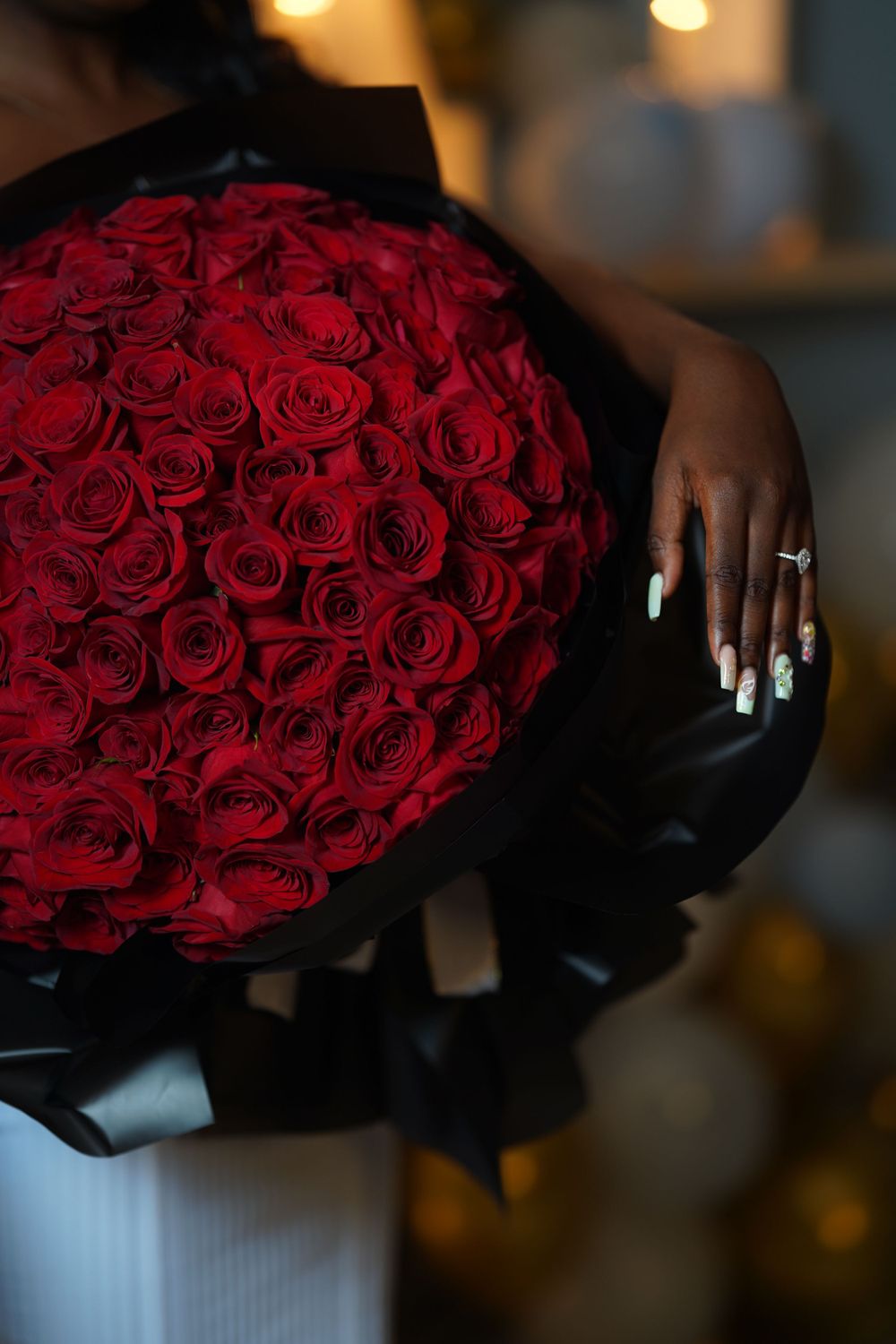 Close-up of a large red rose bouquet with manicured hands and engagement ring visible.