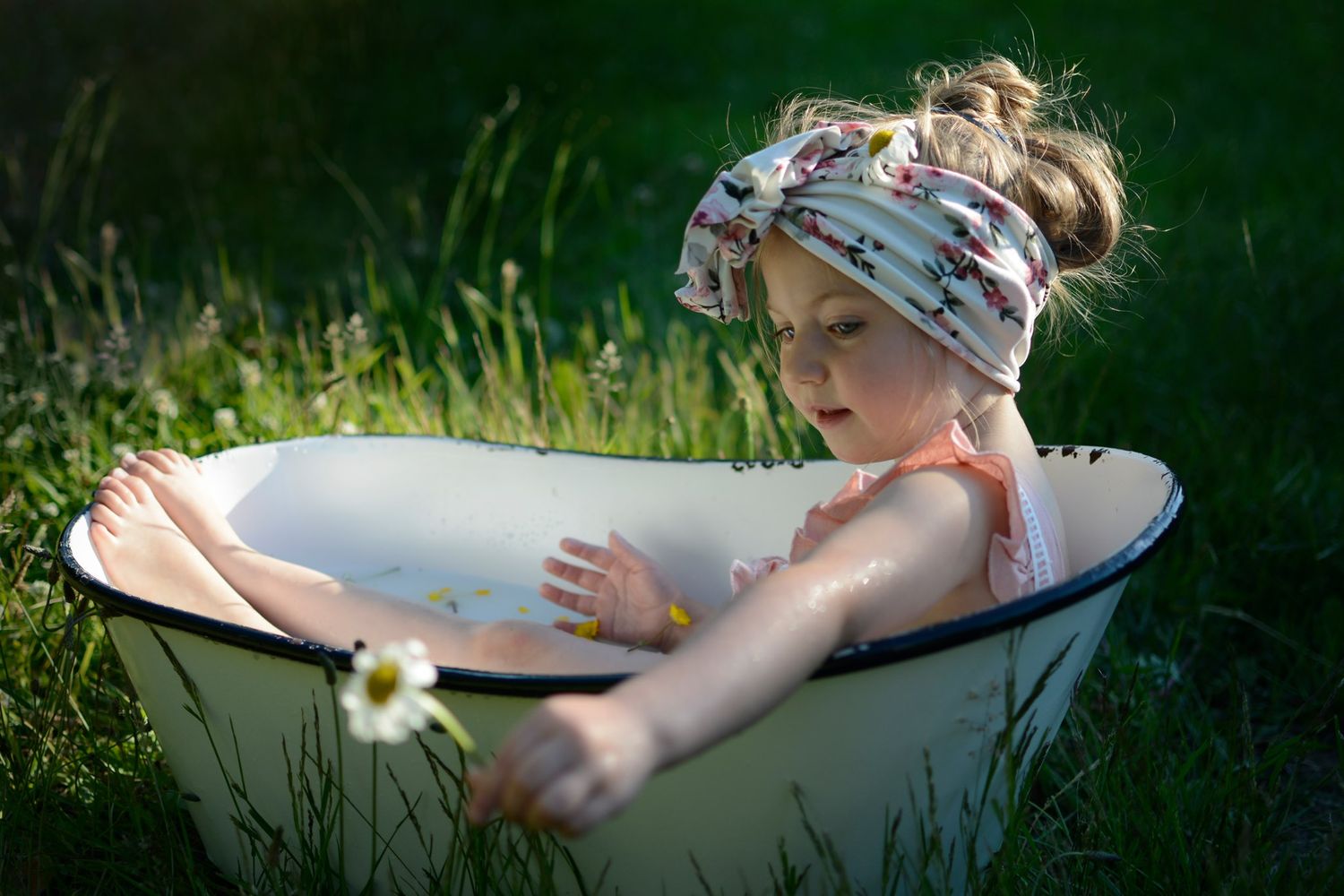 Artistic outdoor bathtub photography session in a grassy field during golden hour.
