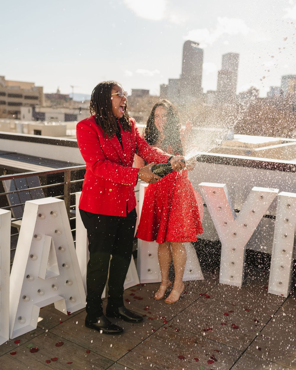 People celebrating on a rooftop with confetti and large white letters visible against city buildings.