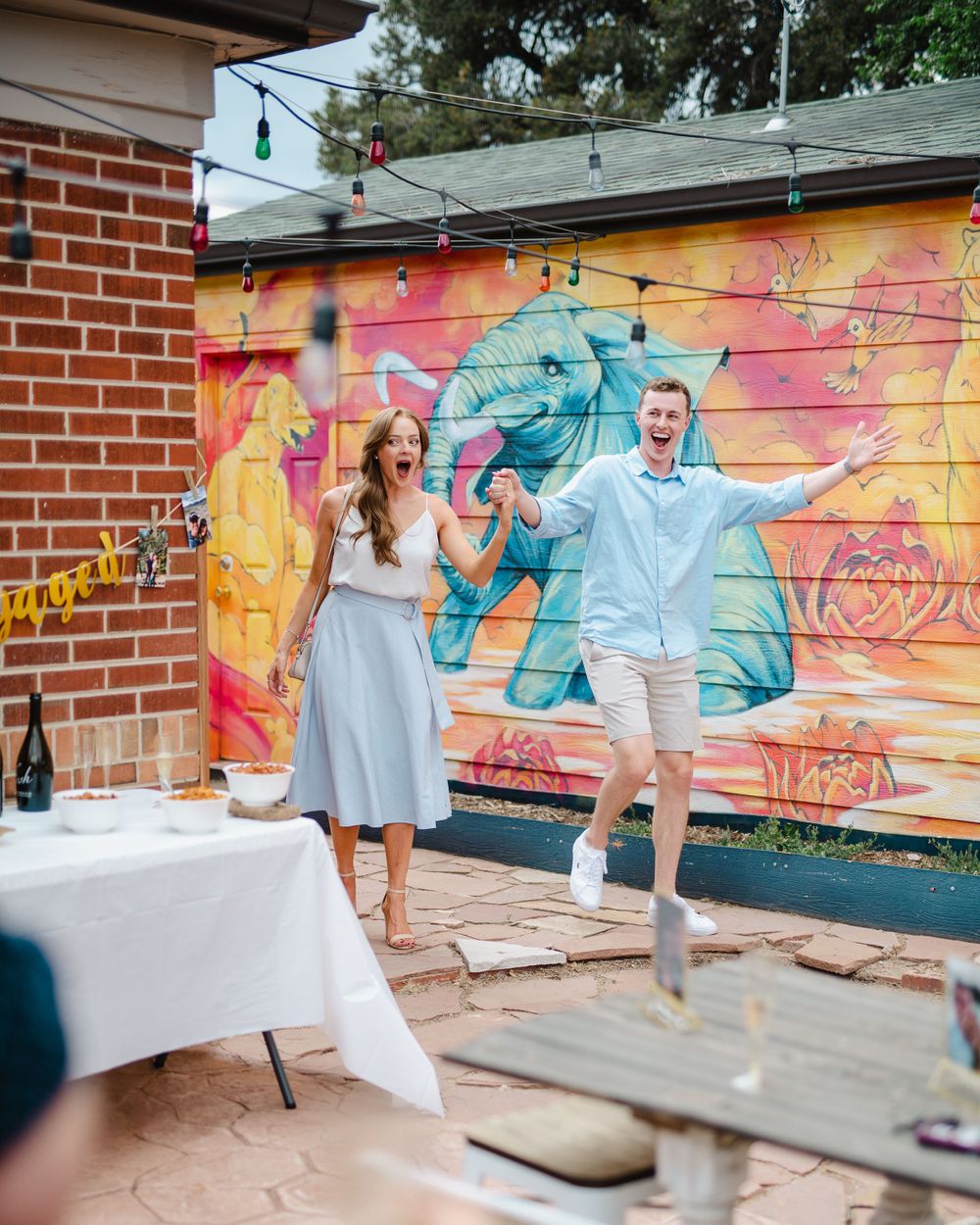 Engaged couple poses playfully in front of colorful street art mural.