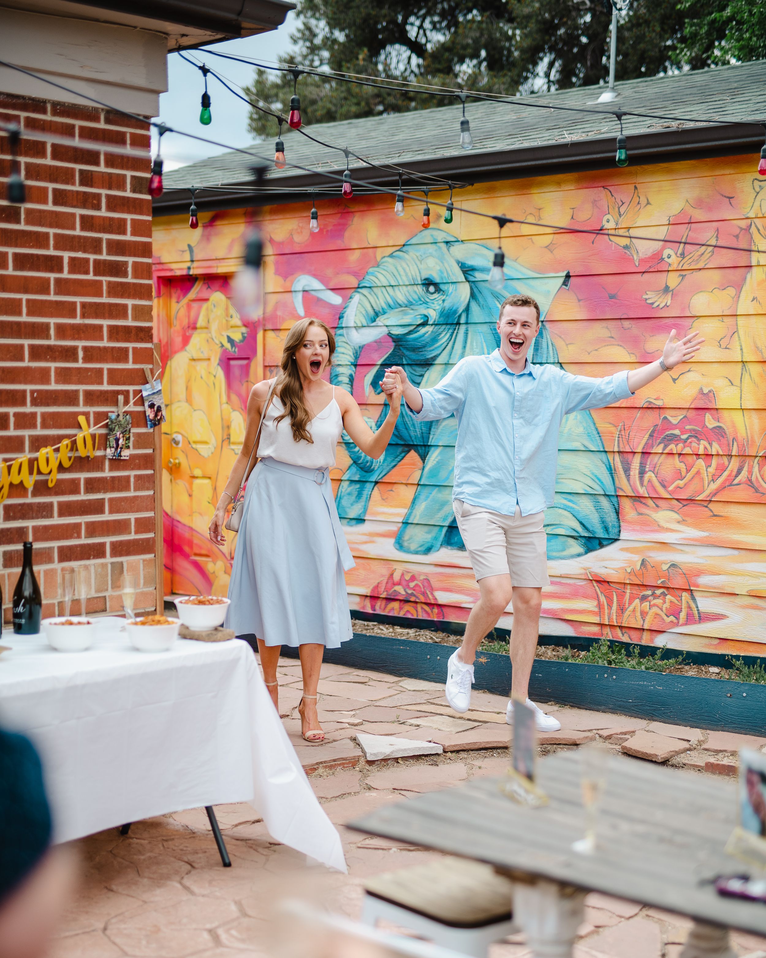Engaged couple poses playfully in front of colorful street art mural.