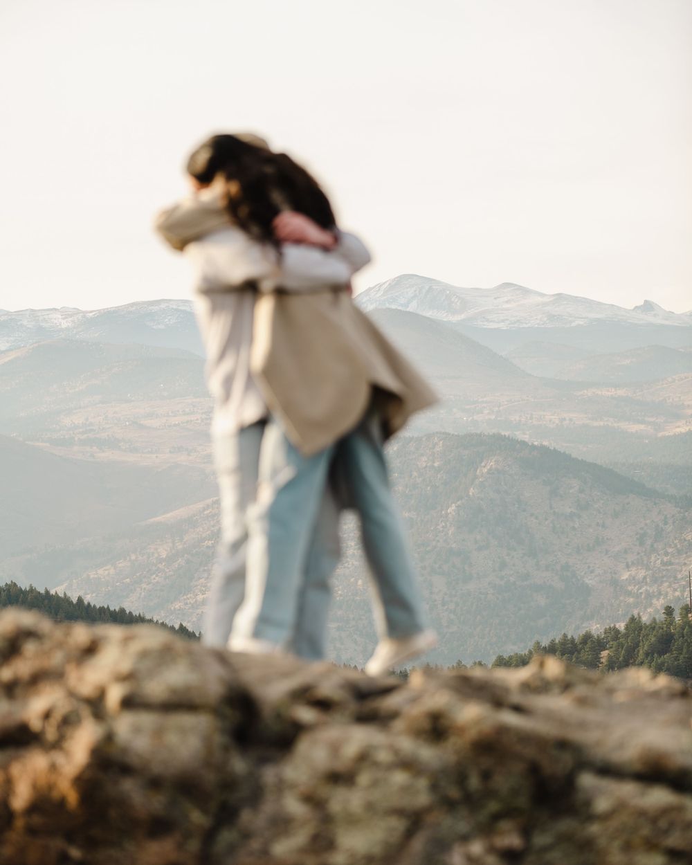 A joyful embrace captured on a mountain summit with misty mountains in the background.