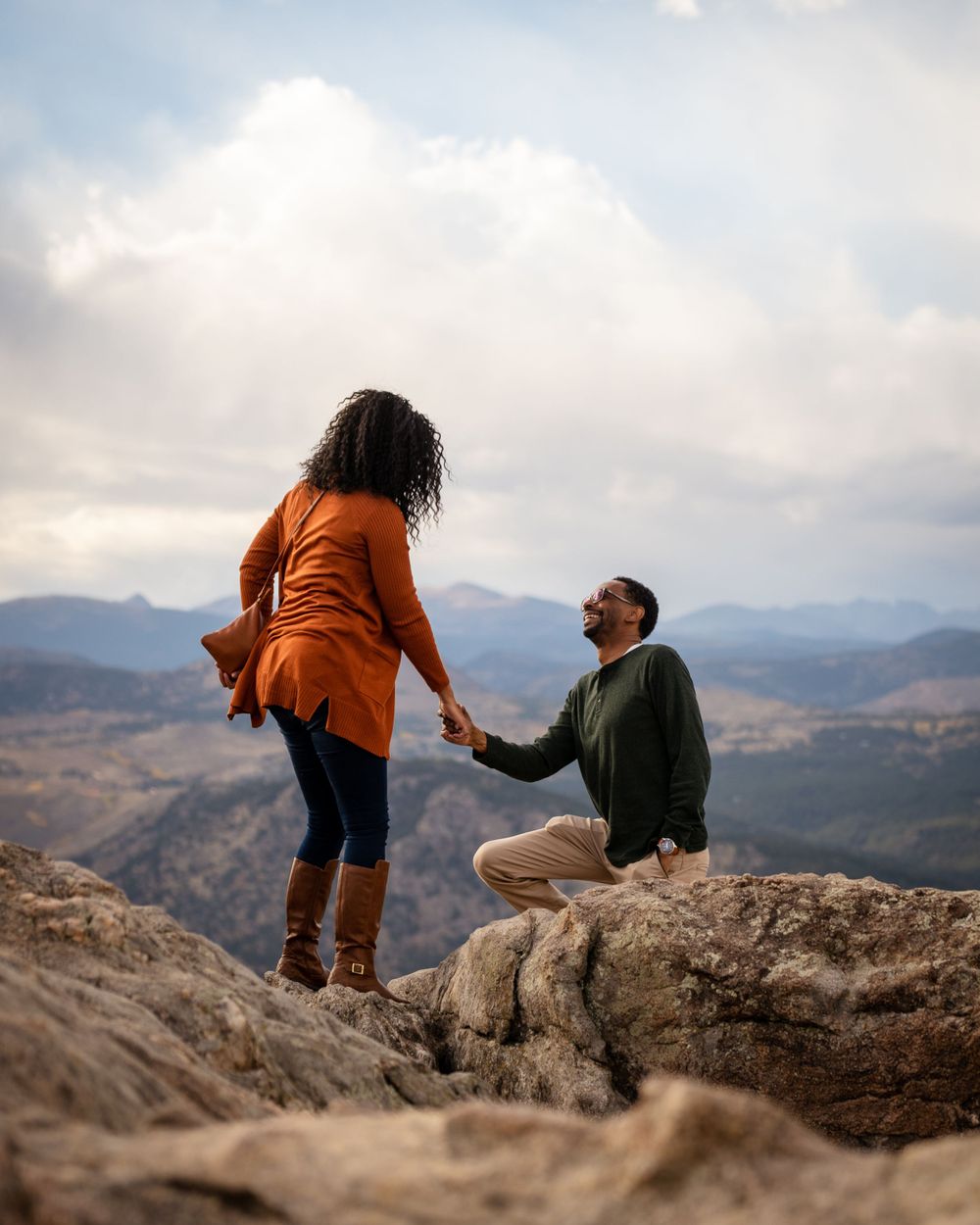 A proposal scene on a mountain cliff with dramatic cloudy skies and vast mountain views.