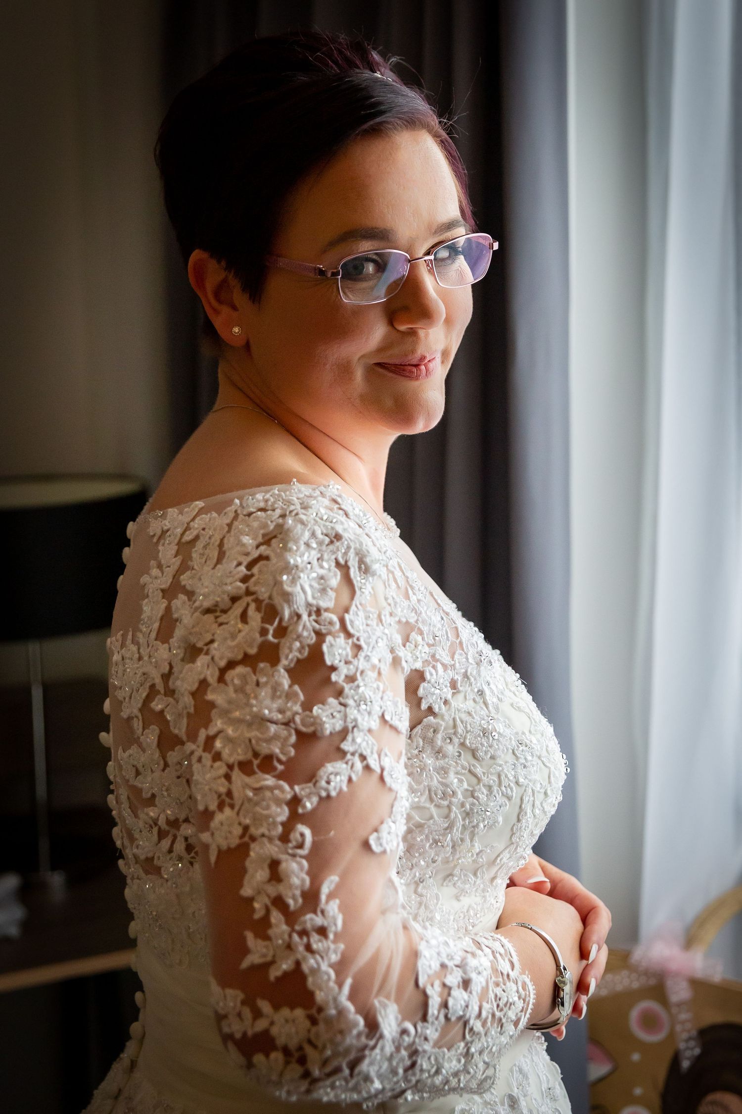Bride in front of a window with a wry smile on her face face during the bridal prep at the Liverpool Crowne Plaza hotel