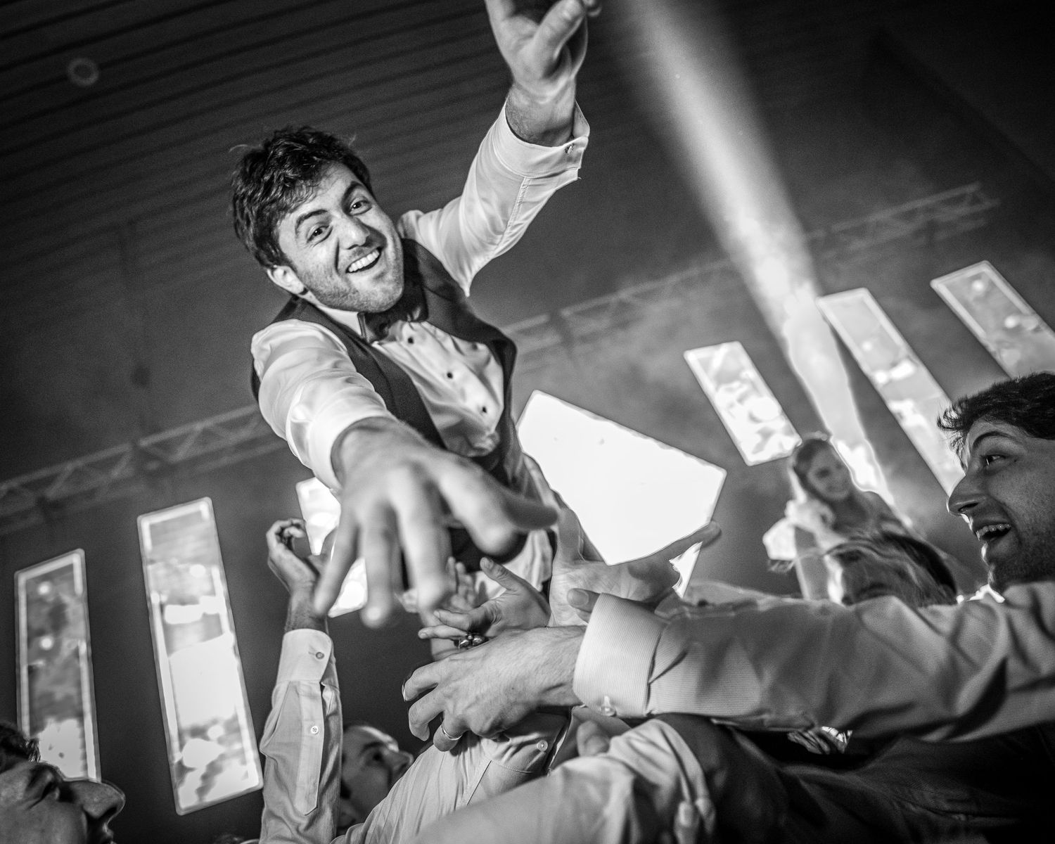 Groom being lifted by guests during lively black and white wedding reception dance.