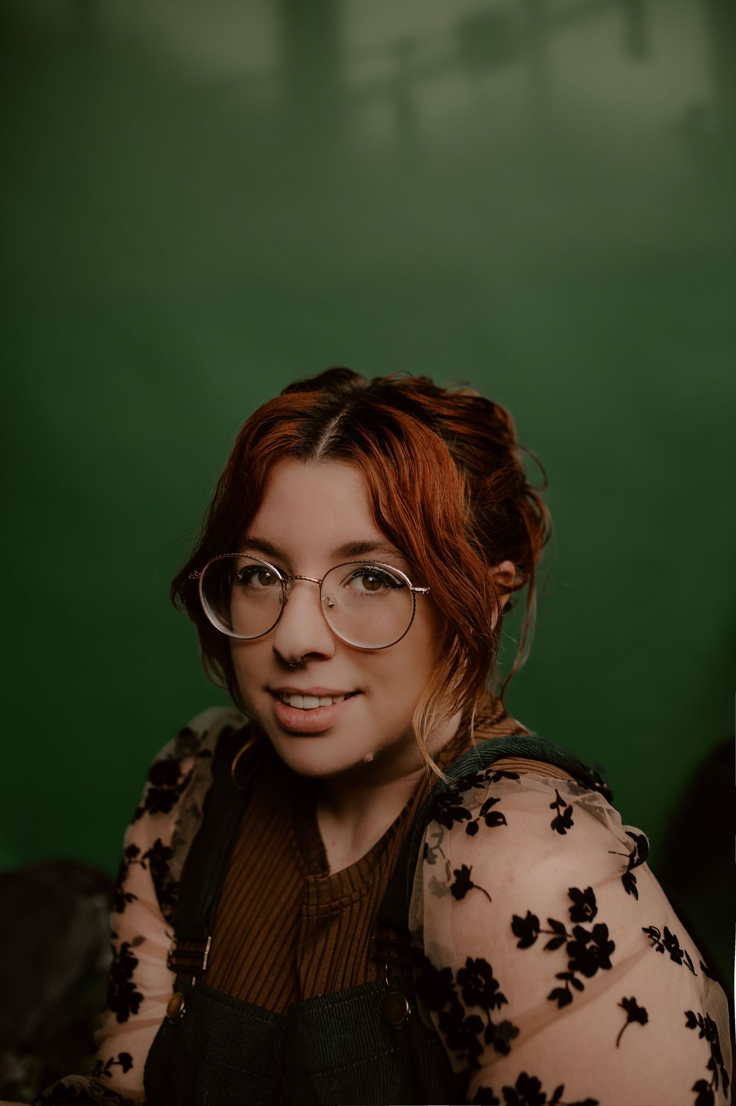A close-up portrait with round glasses and sheer floral overlay against a dark green backdrop.