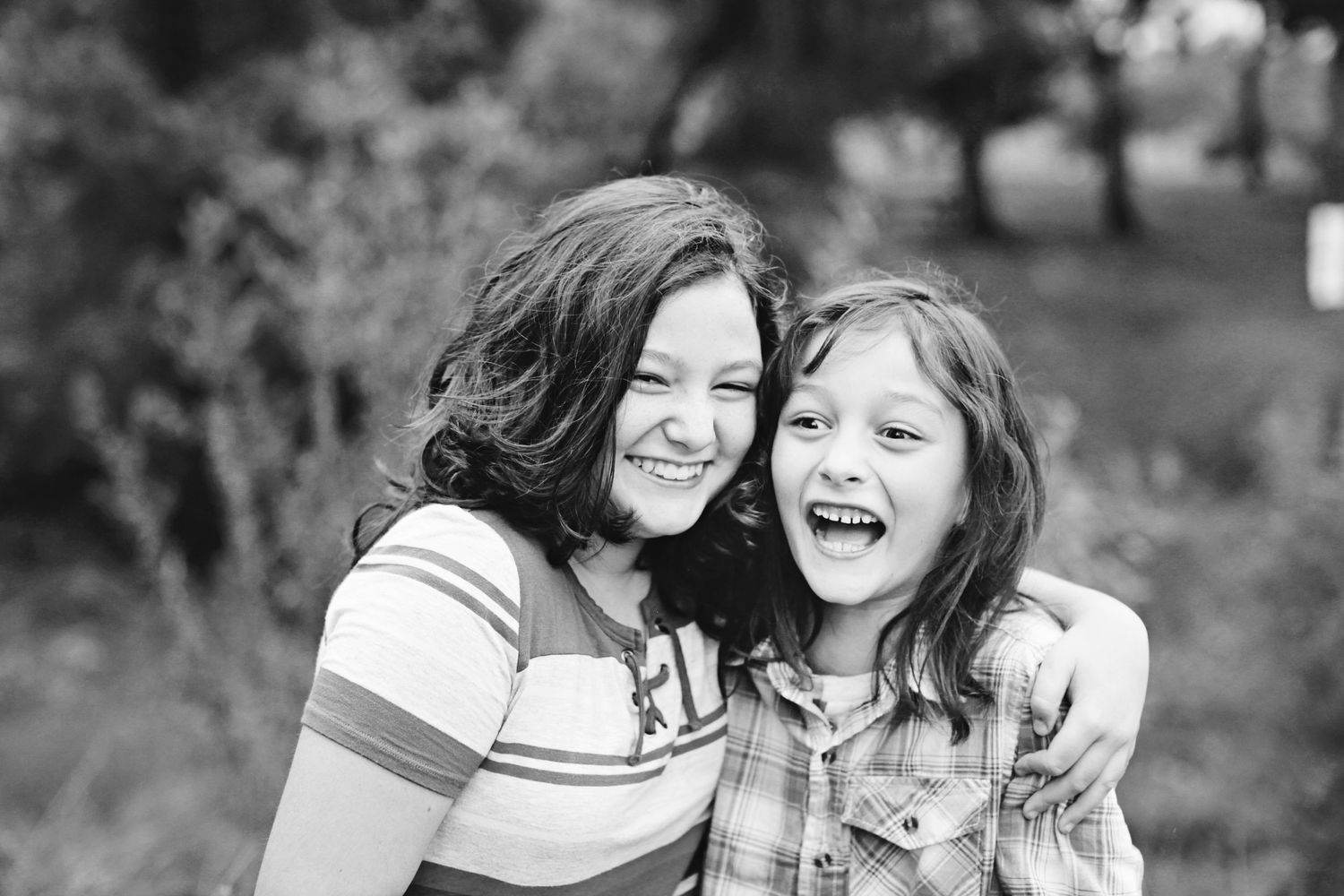Black and white portrait of two people laughing and hugging outdoors.