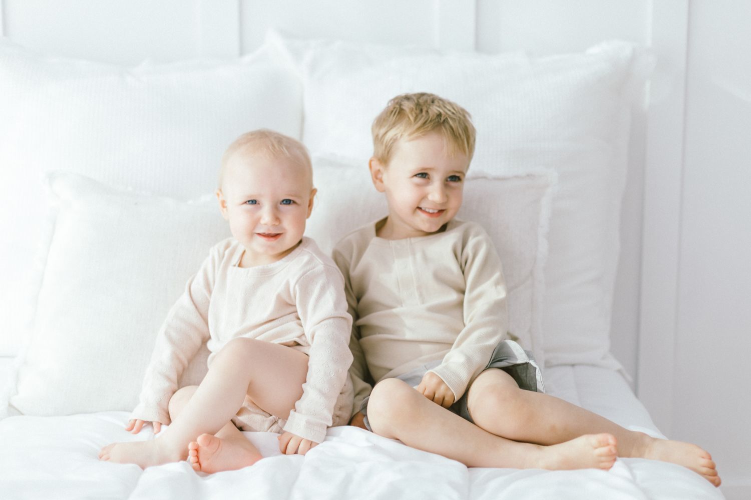 Two young children sitting together on white bedding wearing matching outfits.