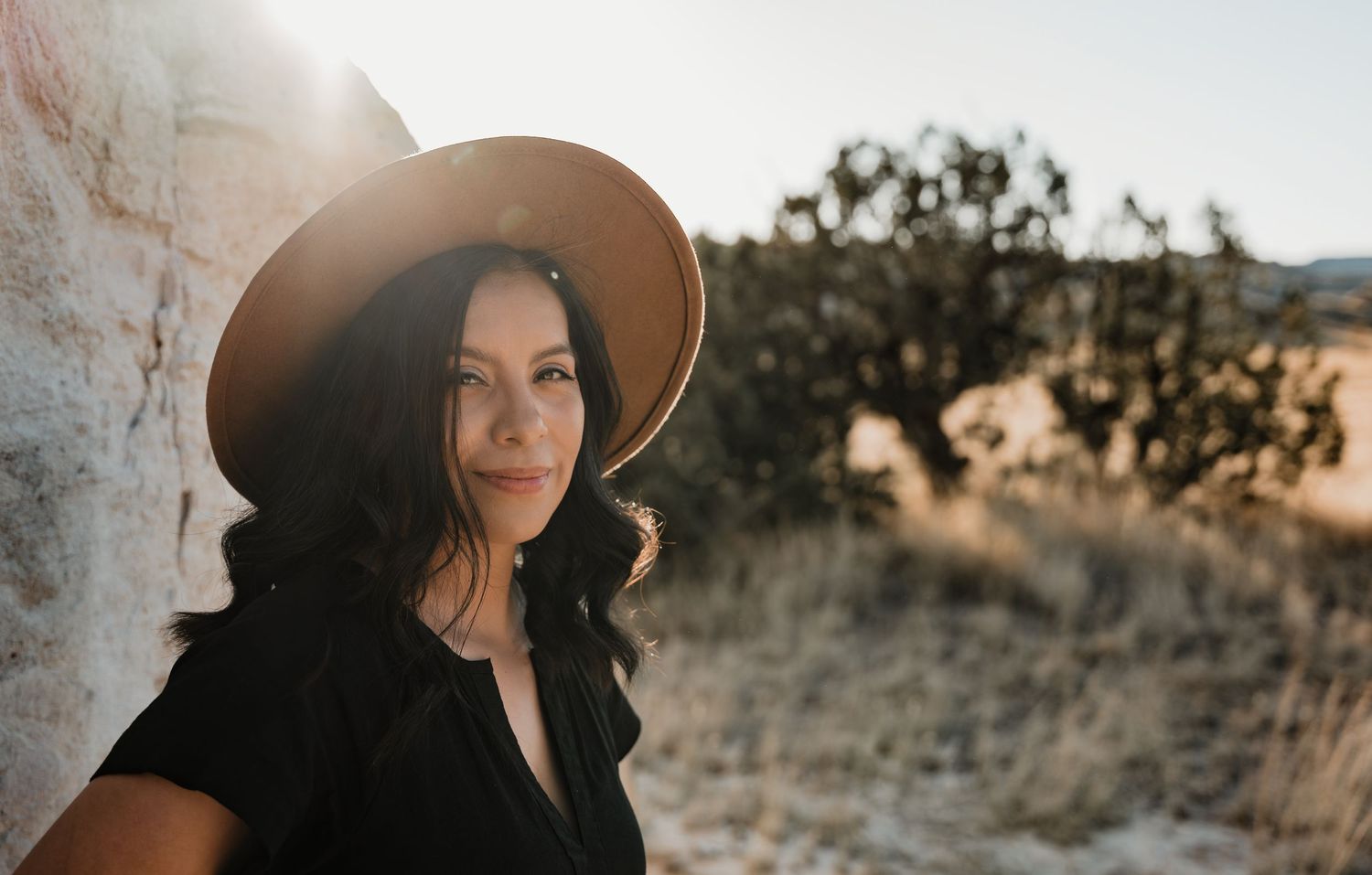 A woman in a brown hat poses against a desert backdrop at golden hour.