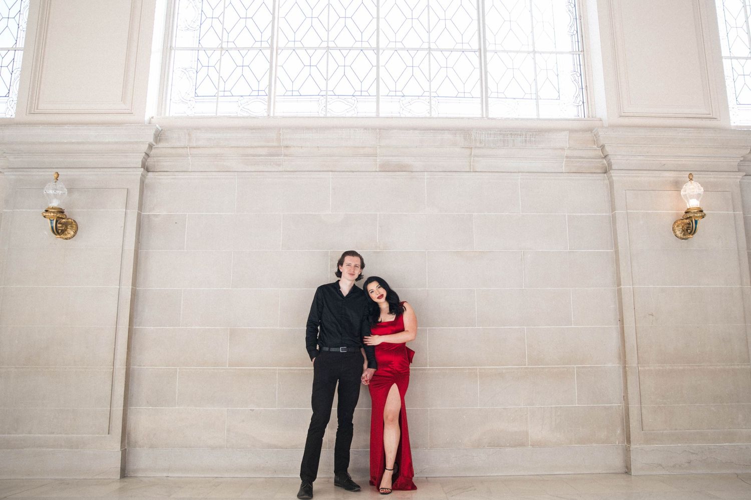 White man in a suit and Mexican Woman in a long red gown stand together embracing in San Francisco City Hall.