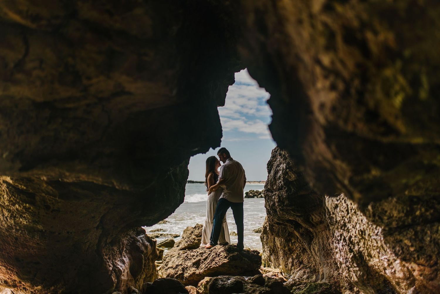Silhouetted couple standing in cave opening with ocean view.