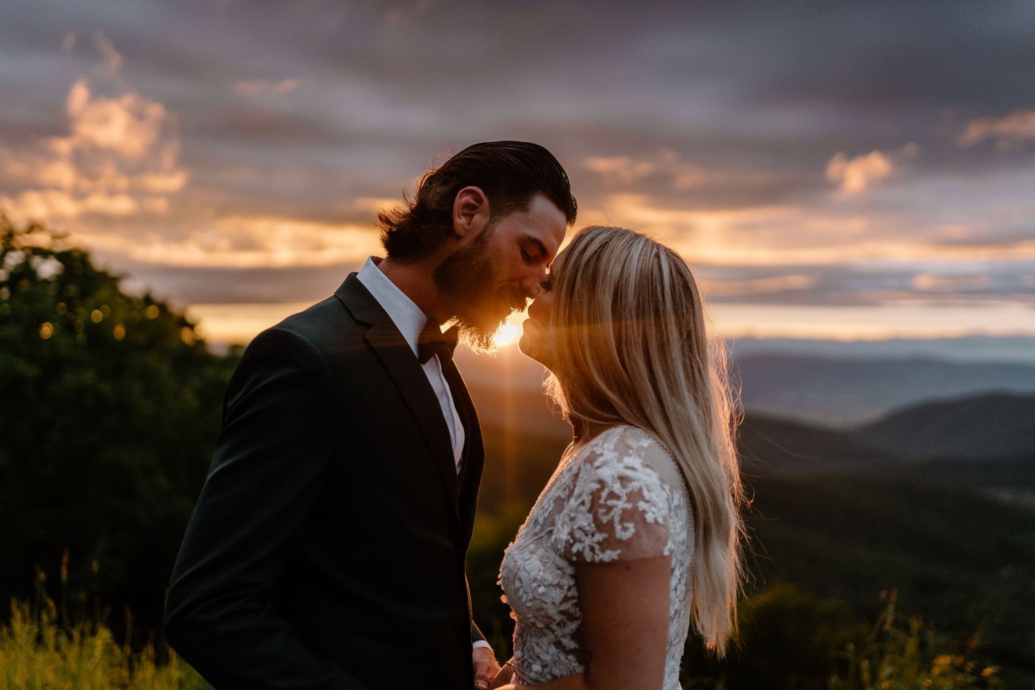 man and woman almost kissing on the side of a mountain at sunset