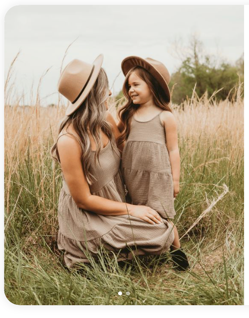 A tender moment captured between two people wearing neutral dresses in a sunlit field of tall grass.