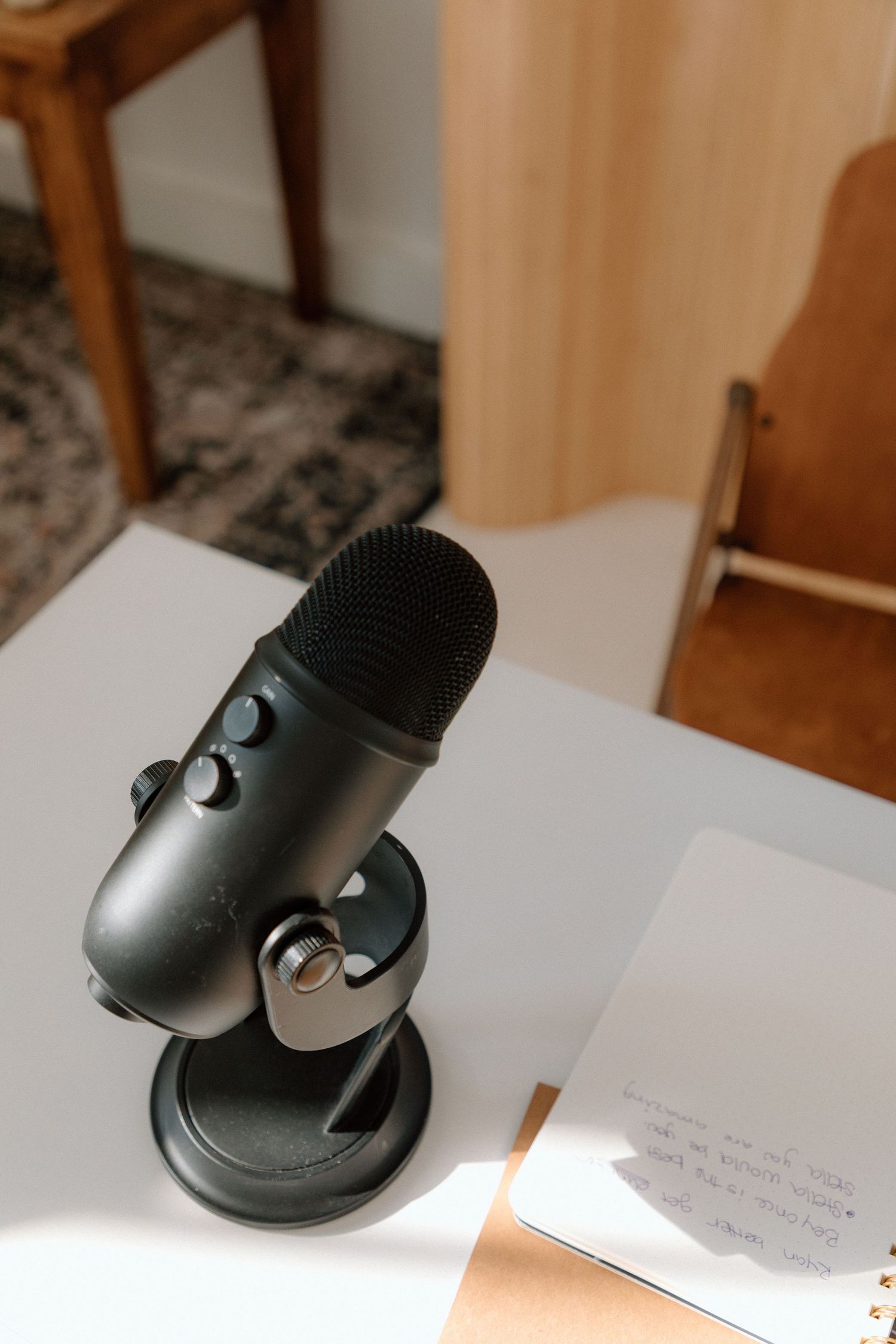Black Blue Yeti microphone sits on white desk with notepad in soft indoor lighting.