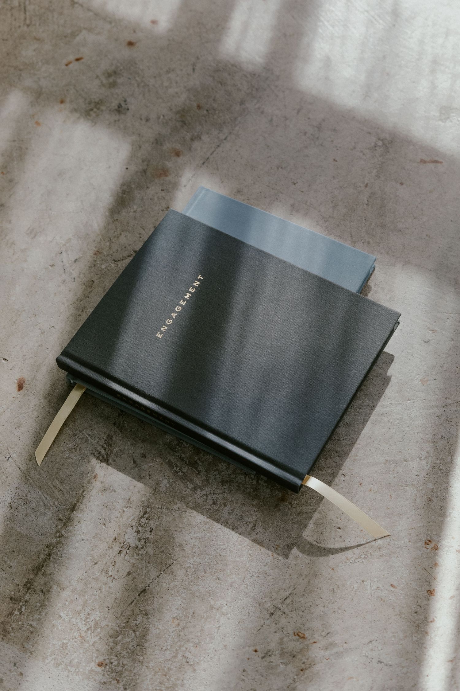 Dark grey engagement journal with bookmark ribbon laying on concrete surface.