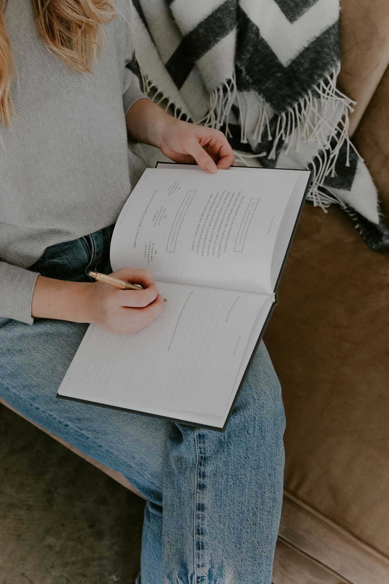 Person reading from an open book while sitting on couch with chevron patterned blanket.