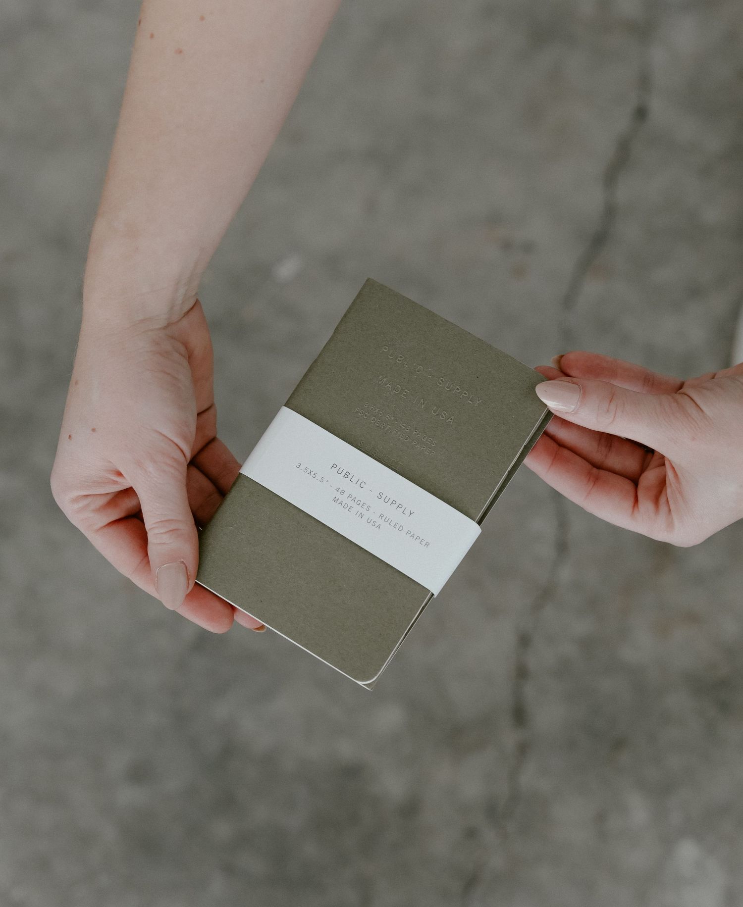 Hands exchanging olive green notebook with white label band.