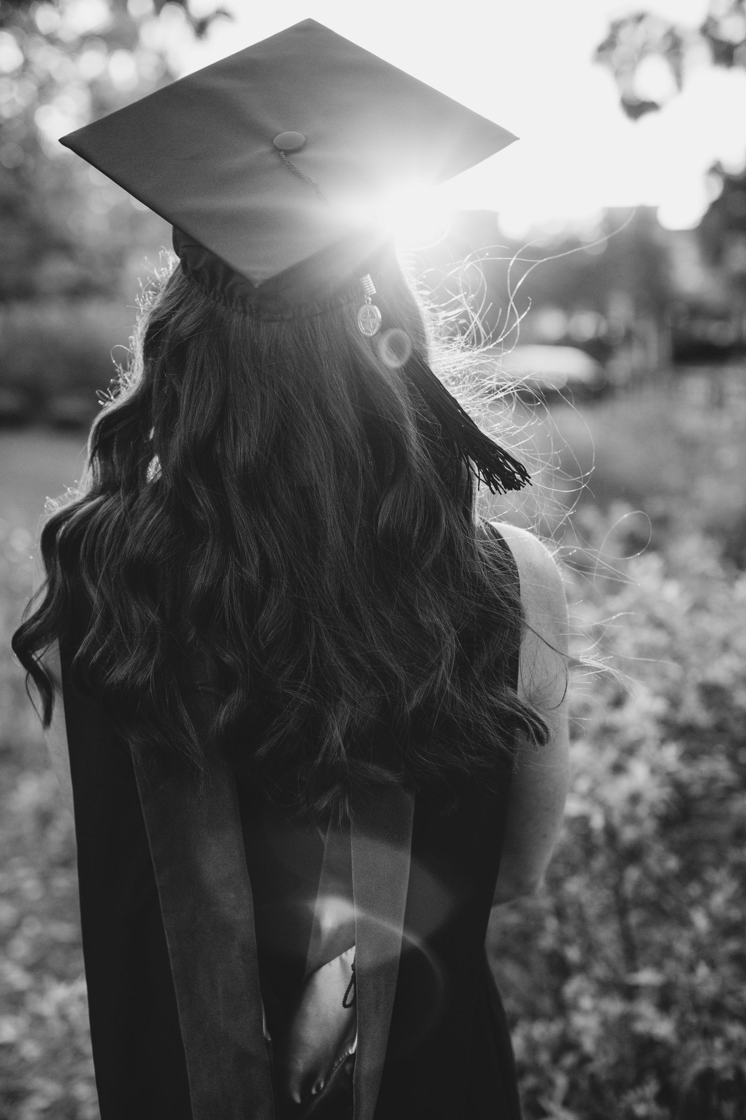 A black and white graduation photo showing a cap and gown silhouette against sunlight.
