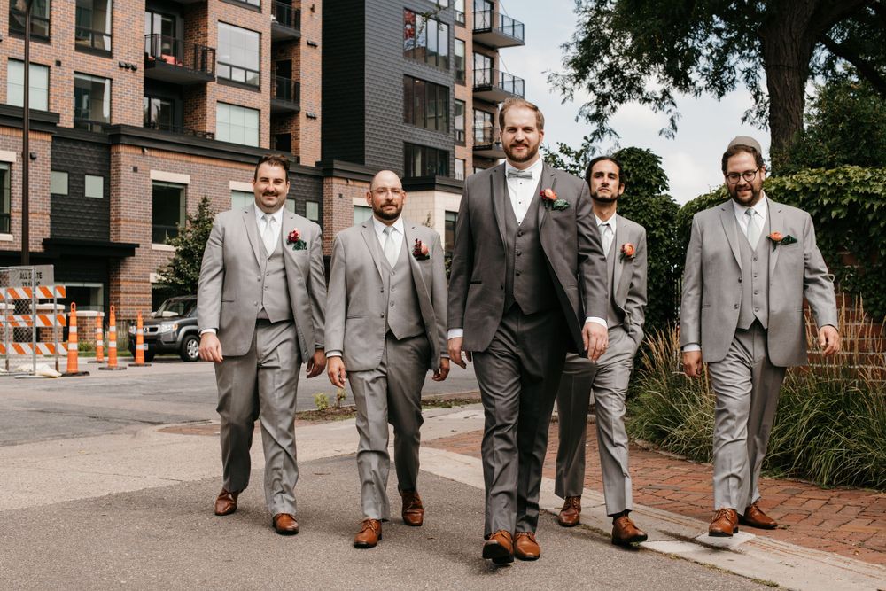 Groom and groomsmen walking confidently in matching gray suits on a city street.